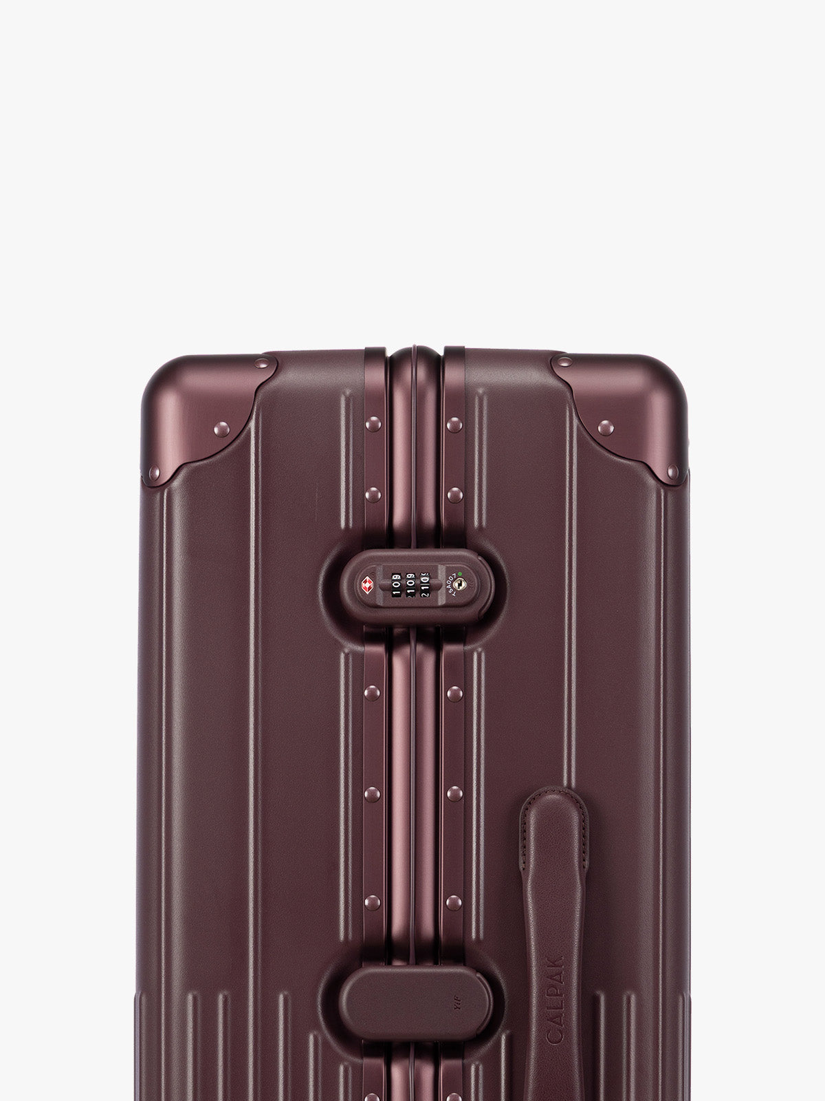 Closeup of TSA-approved lock of CALPAK Large Vault Luggage in deep red Dark Cherry with hard-shell spinner suitcase with a ribbed vertical design, shown from the front on a light gray background; LVT1028-DARK-CHERRY