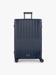 CALPAK Large Vault Luggage in blue Navy with hard-shell spinner suitcase with a ribbed vertical design, shown from the front on a light gray background; LVT1028-NAVY