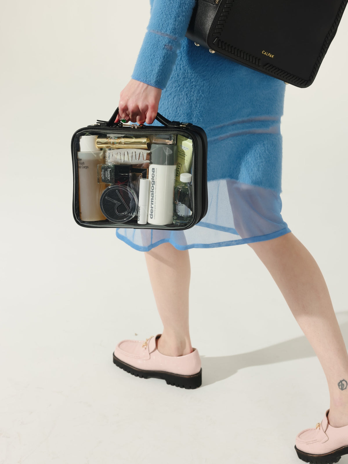 Model holding CALPAK medium transparent makeup case with top handles in black; CMM2201-BLACK