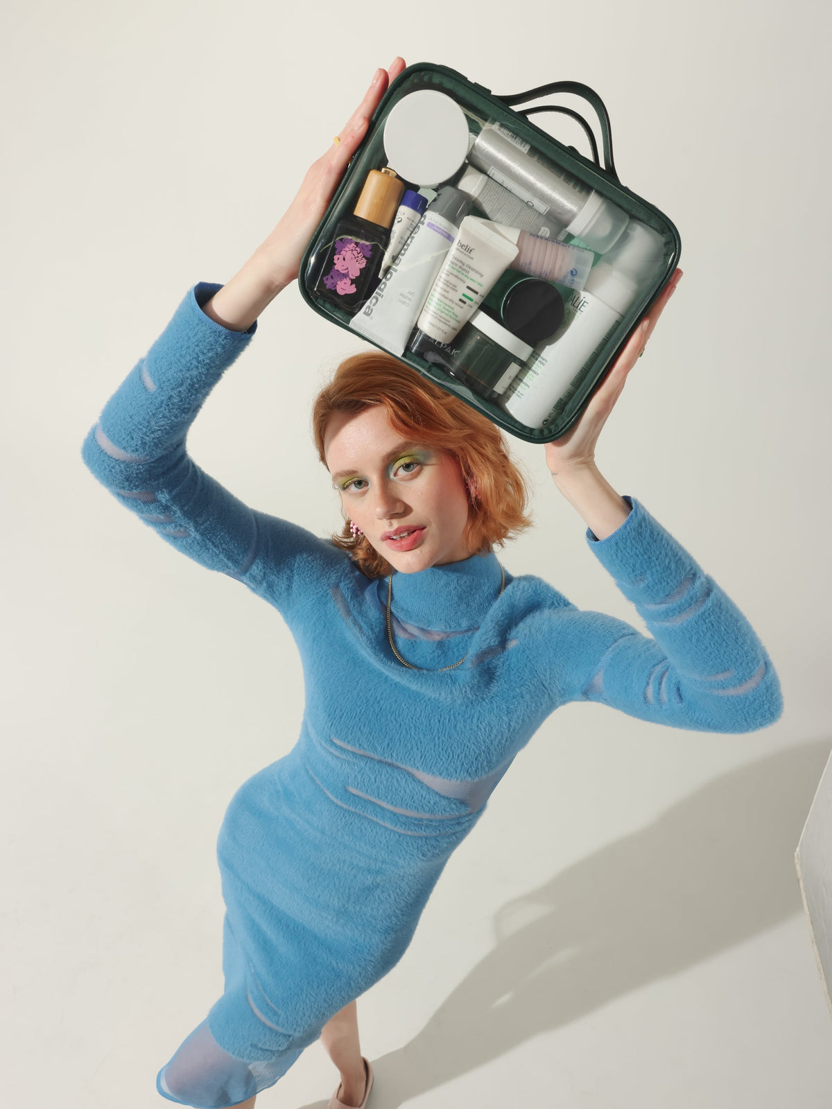 Model holding CALPAK medium transparent makeup case with top handles in emerald; CMM2201-EMERALD