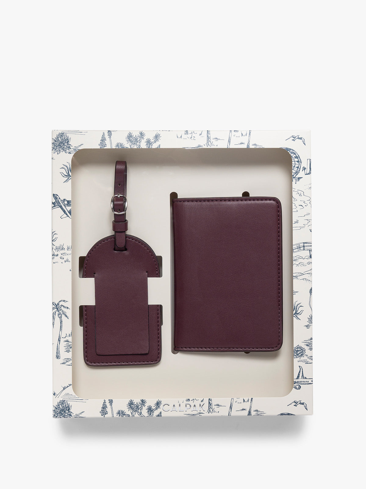 A two-piece CALPAK Luggage Tag and Passport Holder Set in a deep burgundy color, presented inside a blue decorated white gift box; PWTS2601-DARK-CHERRY