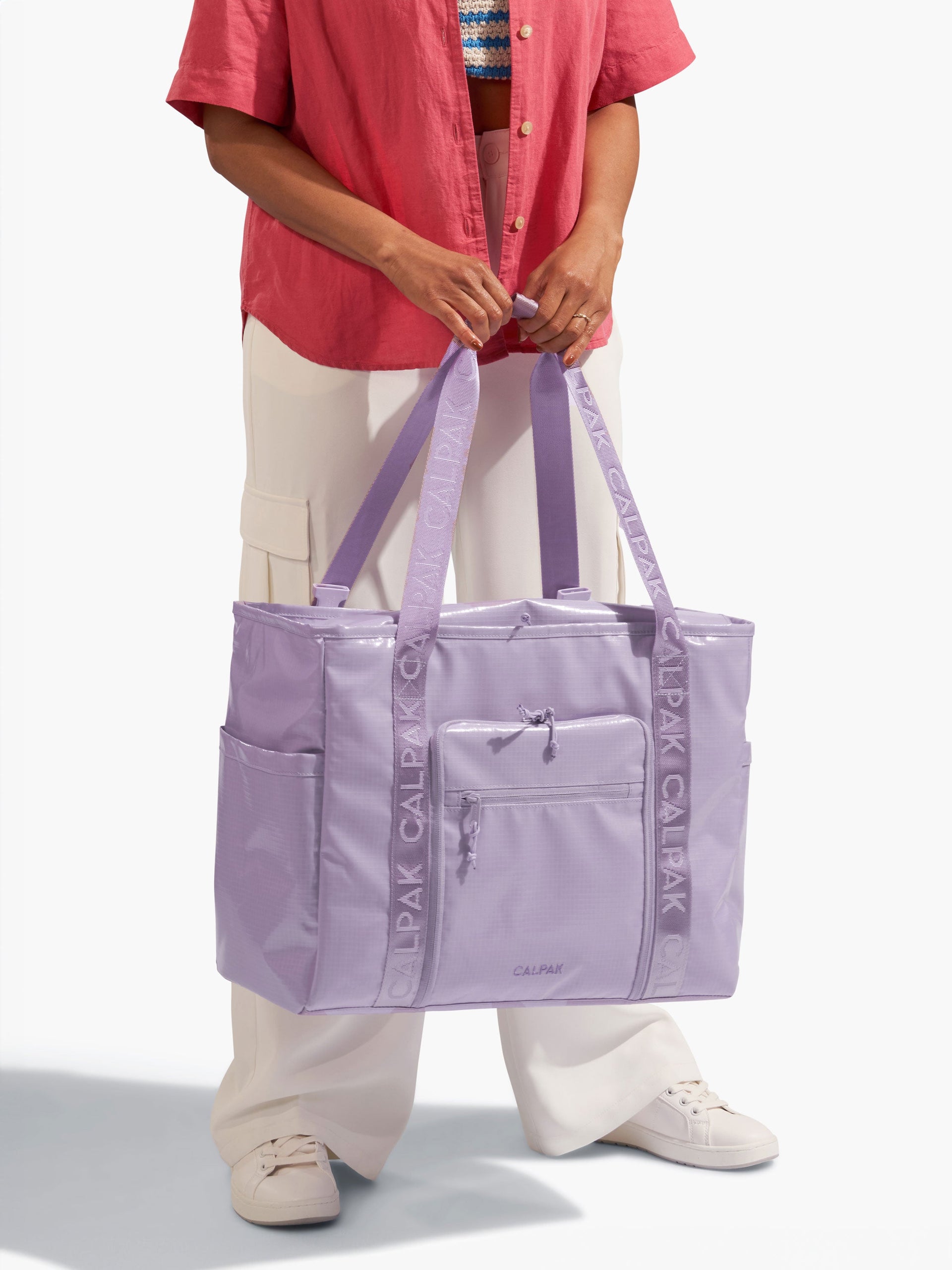 Model holding nylon tote straps of CALPAK Terra 35L Water Resistant Zippered Tote Bag in purple amethyst; TTO2401-AMETHYST