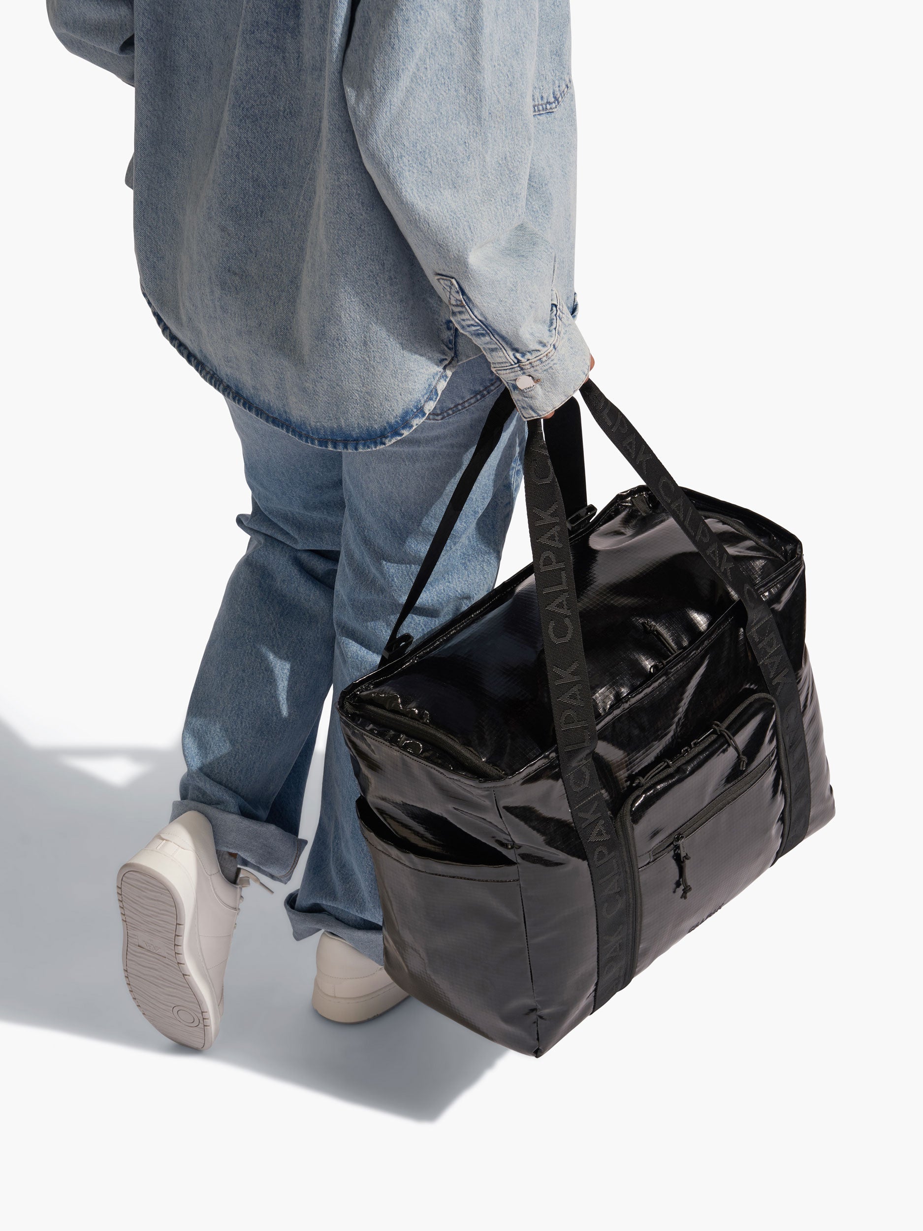 Model holding CALPAK Terra 35L Water Resistant Zippered Tote Bag by durable nylon strap in black; TTO2401-OBSIDIAN