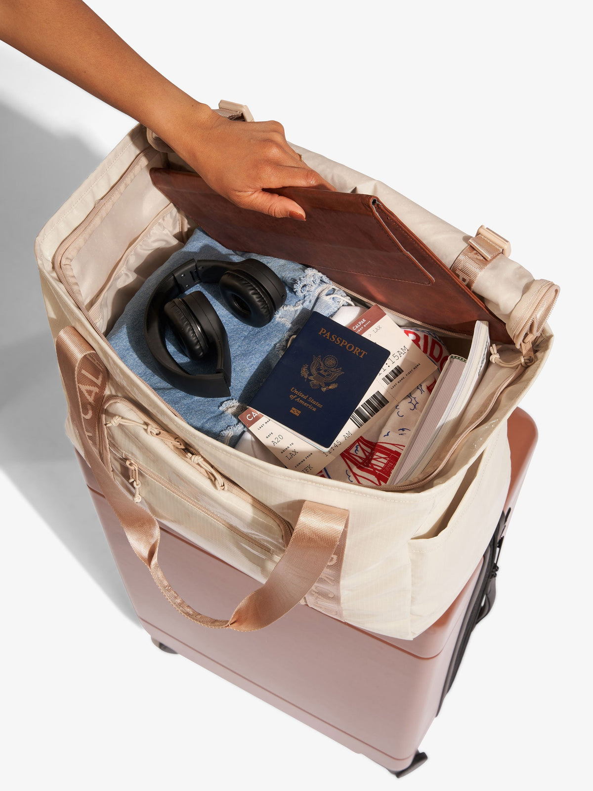 Beige CALPAK Terra 35L Water Resistant Zippered Tote Bag with travel items inside interior; TTO2401-WHITE-SANDS