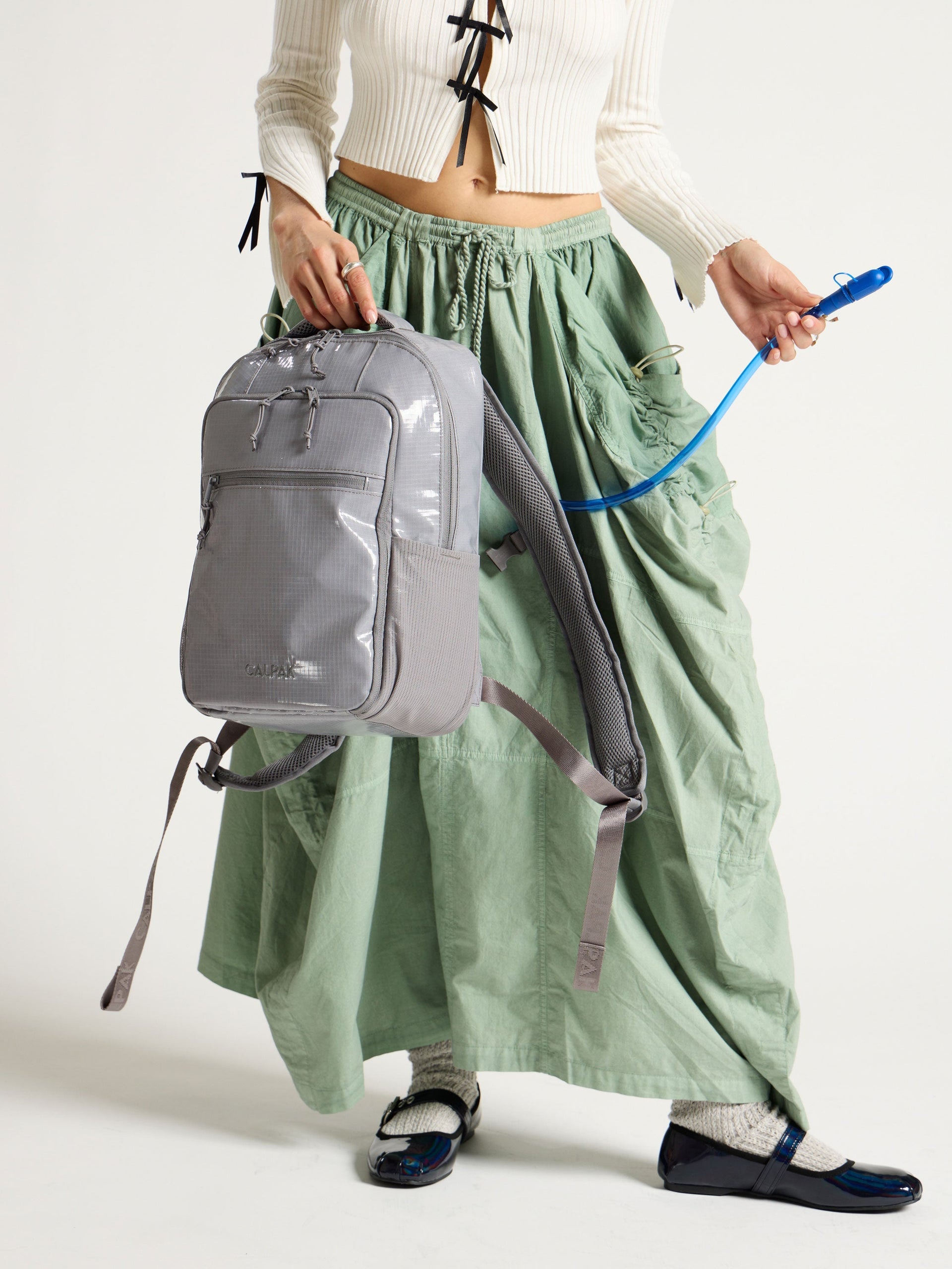 Model displaying straw of removable hydration reservoir in gray CALPAK Terra Hydration Backpack; BPT2201-STORM