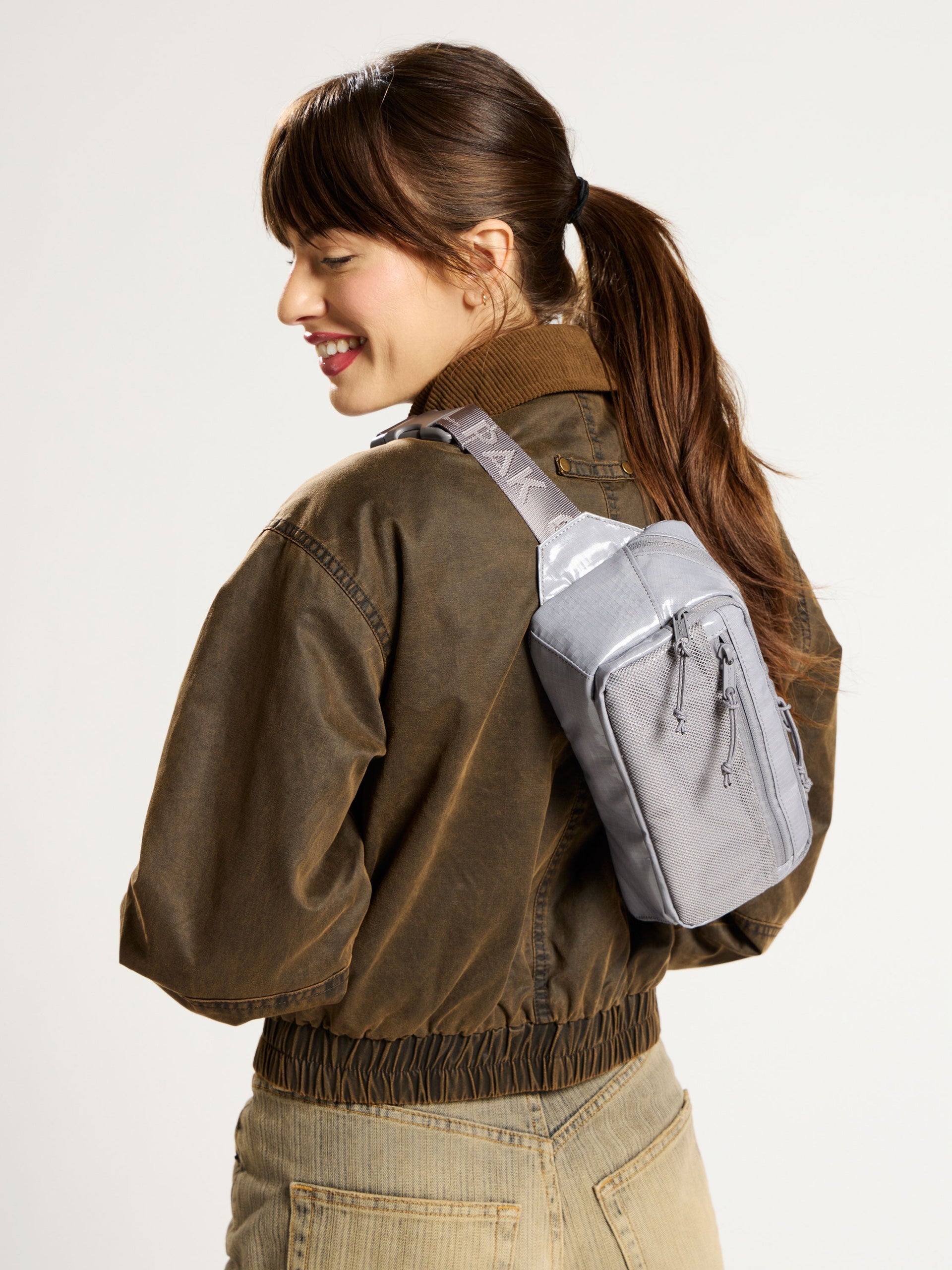 Model wearing gray CALPAK Terra Small Sling Bag as crossbody bag; BBT2301-STORM