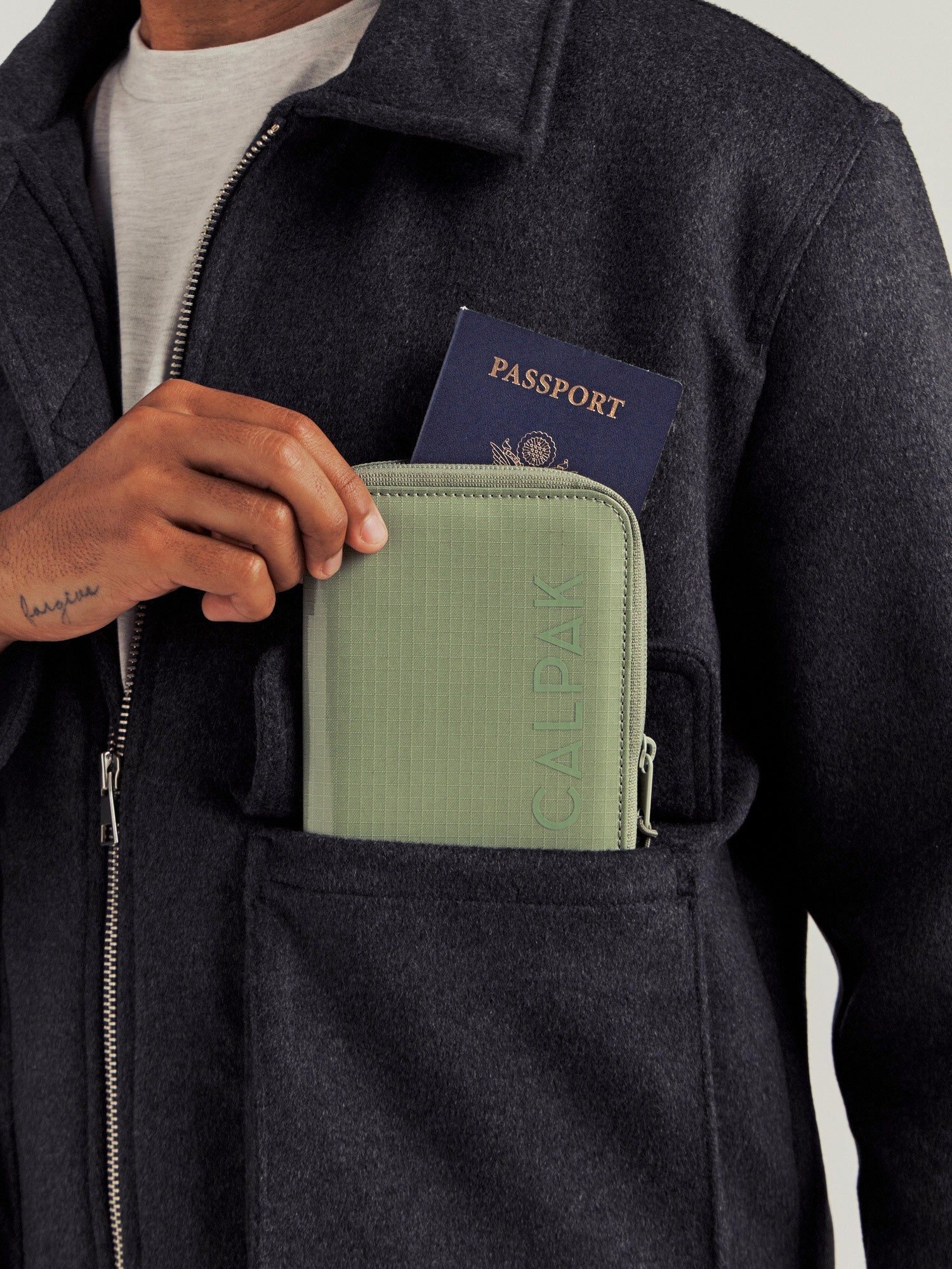 CALPAK Terra Zippered Passport Wallet in Juniper with passport being placed inside a model's jacket pocket; ATPW2501-JUNIPER