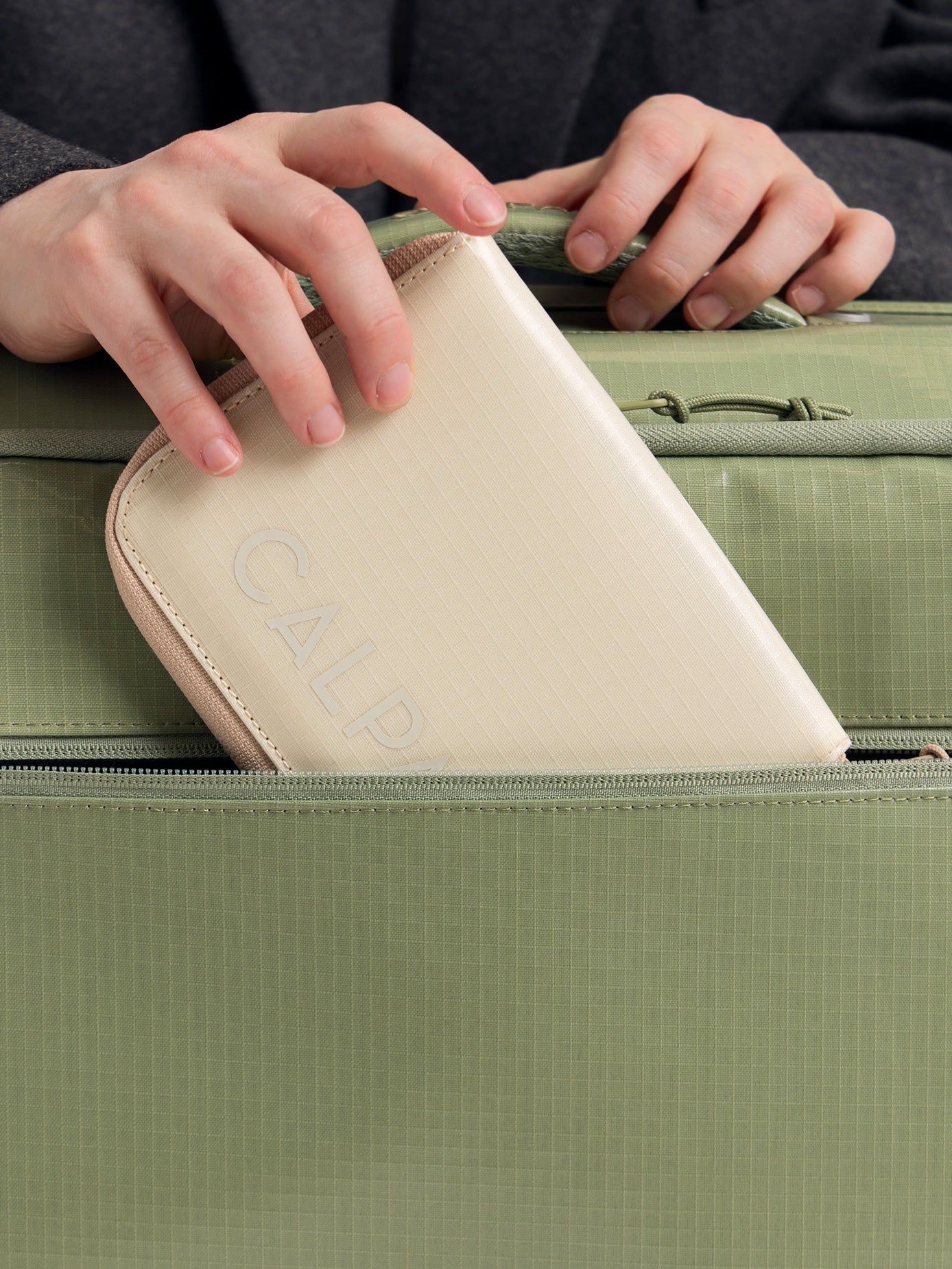 CALPAK Terra Zippered Passport Wallet in beige White Sands with passport being placed inside a bag; ATPW2501-WHITE-SANDS