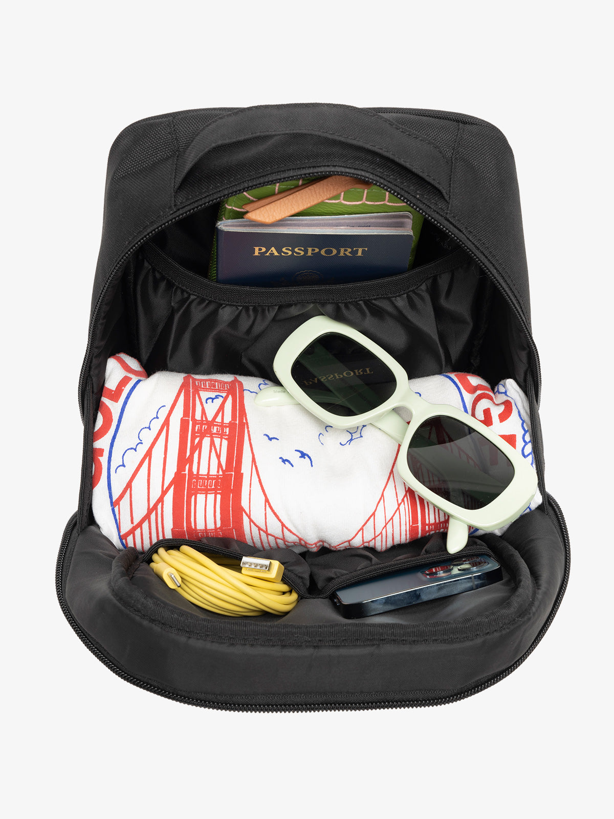 Interior view of black CALPAK The Everything Cube with notebook and passport in large slip pocket, cords and phone in front slip pockets, and sunglasses and t-shirt in main compartment; ACE2401-BLACK