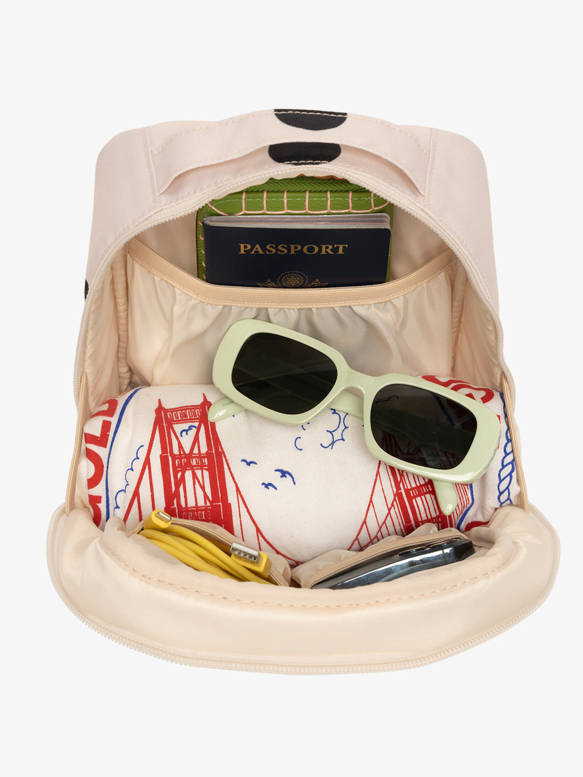 Interior view of polka dot CALPAK The Everything Cube with notebook and passport in large slip pocket, cords and phone in front slip pockets, and sunglasses and t-shirt in main compartment; ACE2401-POLKA-DOT