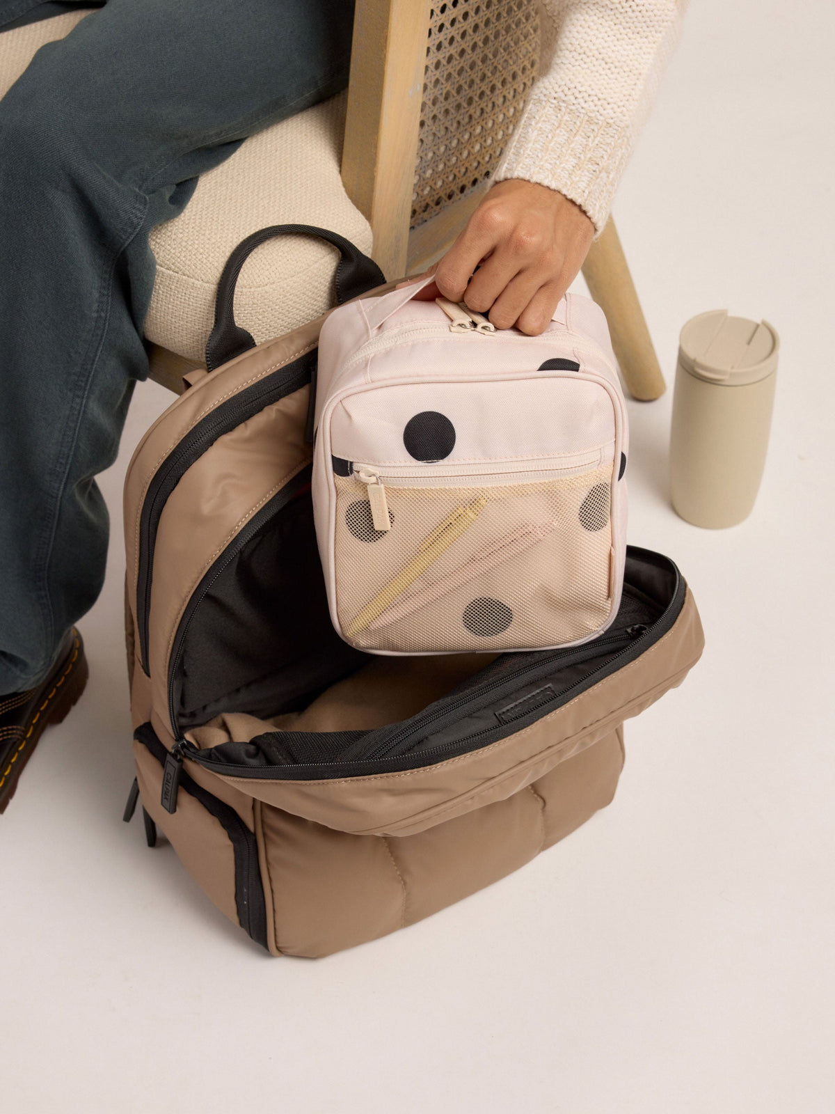 Model placing passport inside front mesh pocket of polka dot CALPAK The Everything Cube; ACE2401-POLKA-DOT