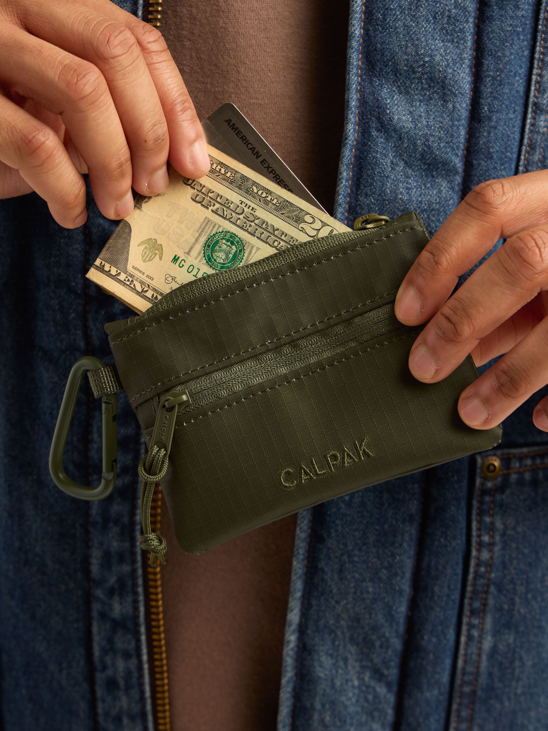 Model adding money in the CALPAK Terra Clippable Card Pouch in dark green Matte Pine front view; TPC2401-PINE