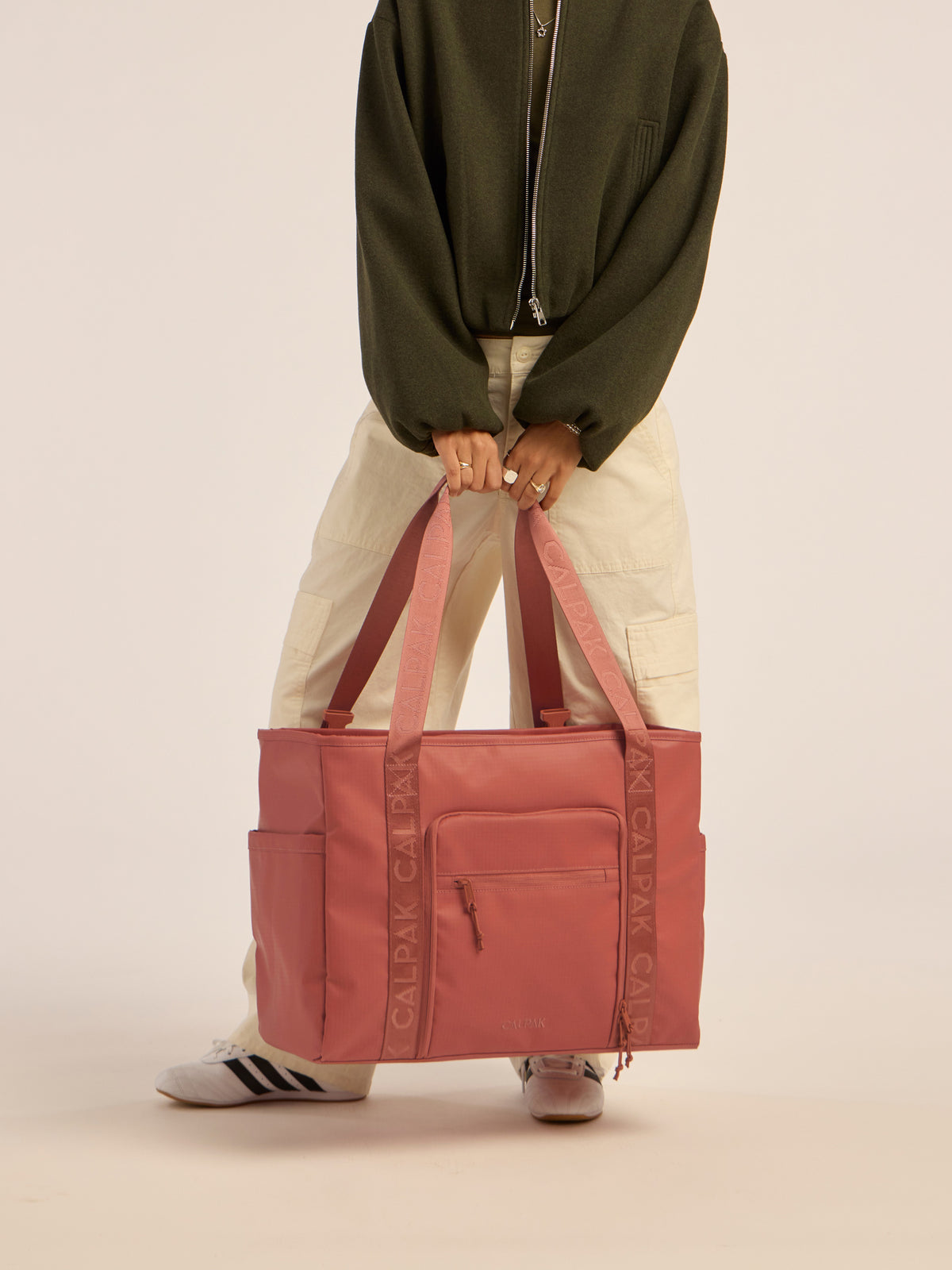 Model holding the CALPAK Terra 35L Water Resistant Zippered Tote Bag in red and orange Matte Clay;TTO2401-CLAY