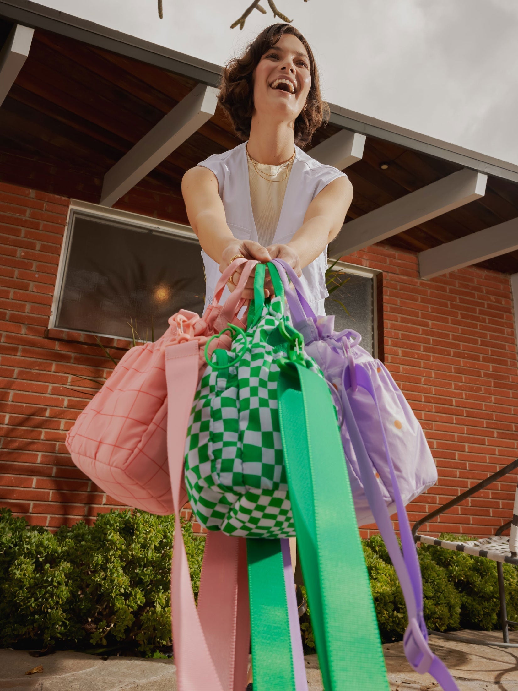 Model carrying CALPAK Water Bottle Holders with detachable sling, top handles and zipped front pocket in pink grid, green checkerboard and purple floral print ; AWH2101-ORCHID-FIELDS