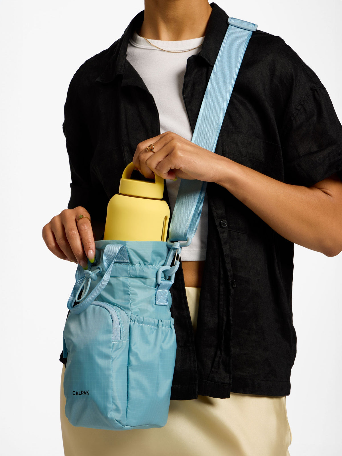 Model wearing CALPAK Water Bottle Holder with crossbody strap in powder blue; AWH2101-POWDER-BLUE