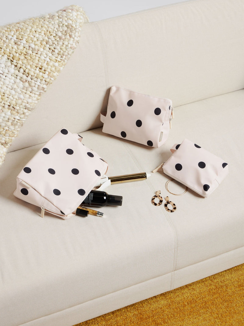 A polka-dot dopp kit set arranged on a neutral sofa, paired with beauty essentials like lip gloss and perfume