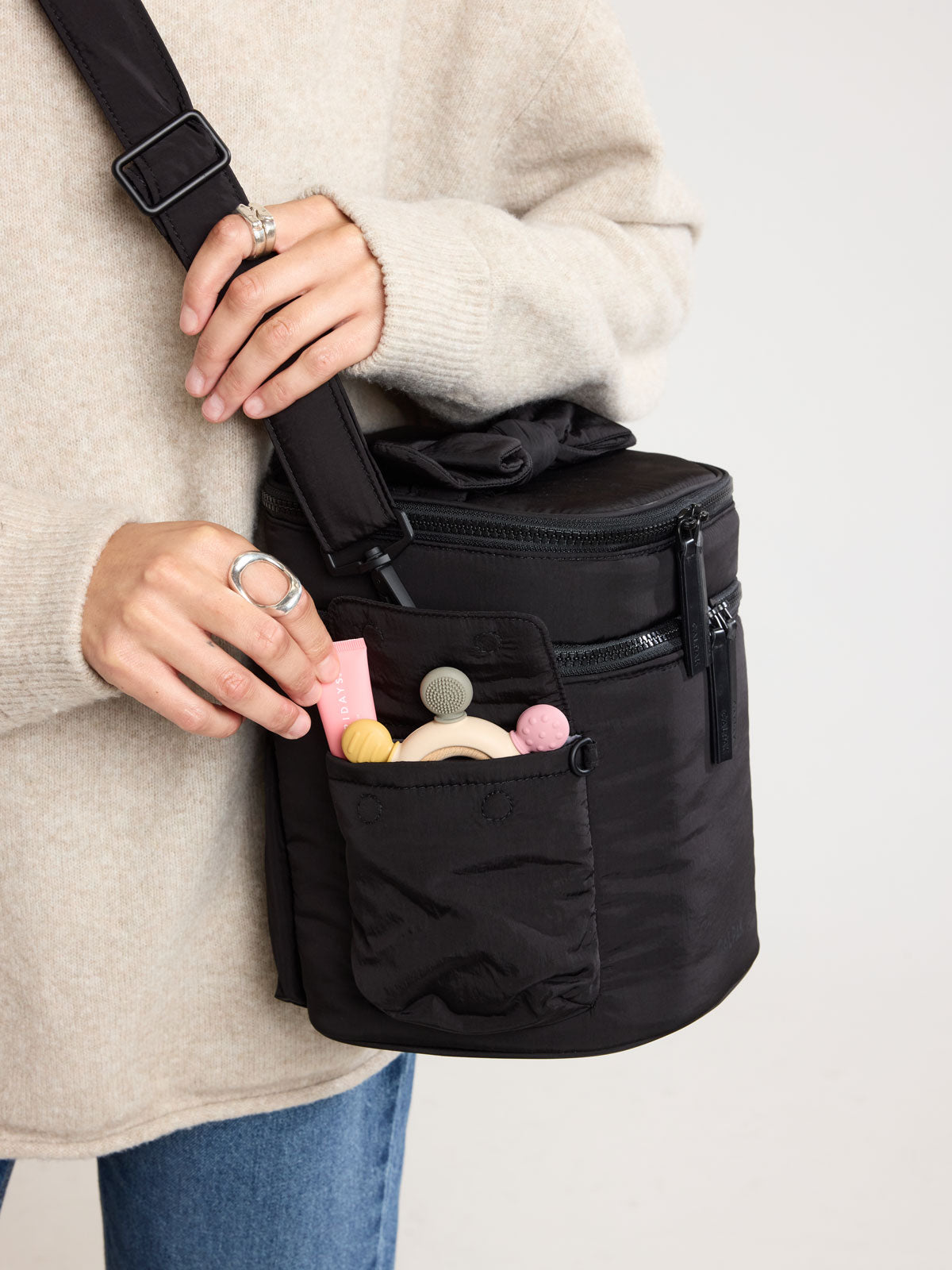 Woman putting items in the side pocket of CALPAK Insulated Baby Bottle Bag in Black; IBB2601-BLACK