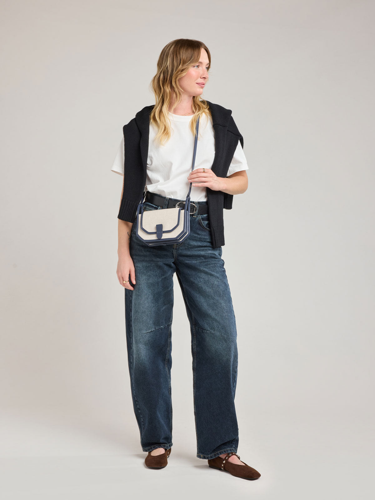 Woman wearing CALPAK Colette Canvas Crossbody Wallet Bag in Natural Brown with beige canvas material and blue finishing; CLWC2601-NATURAL-NAVY