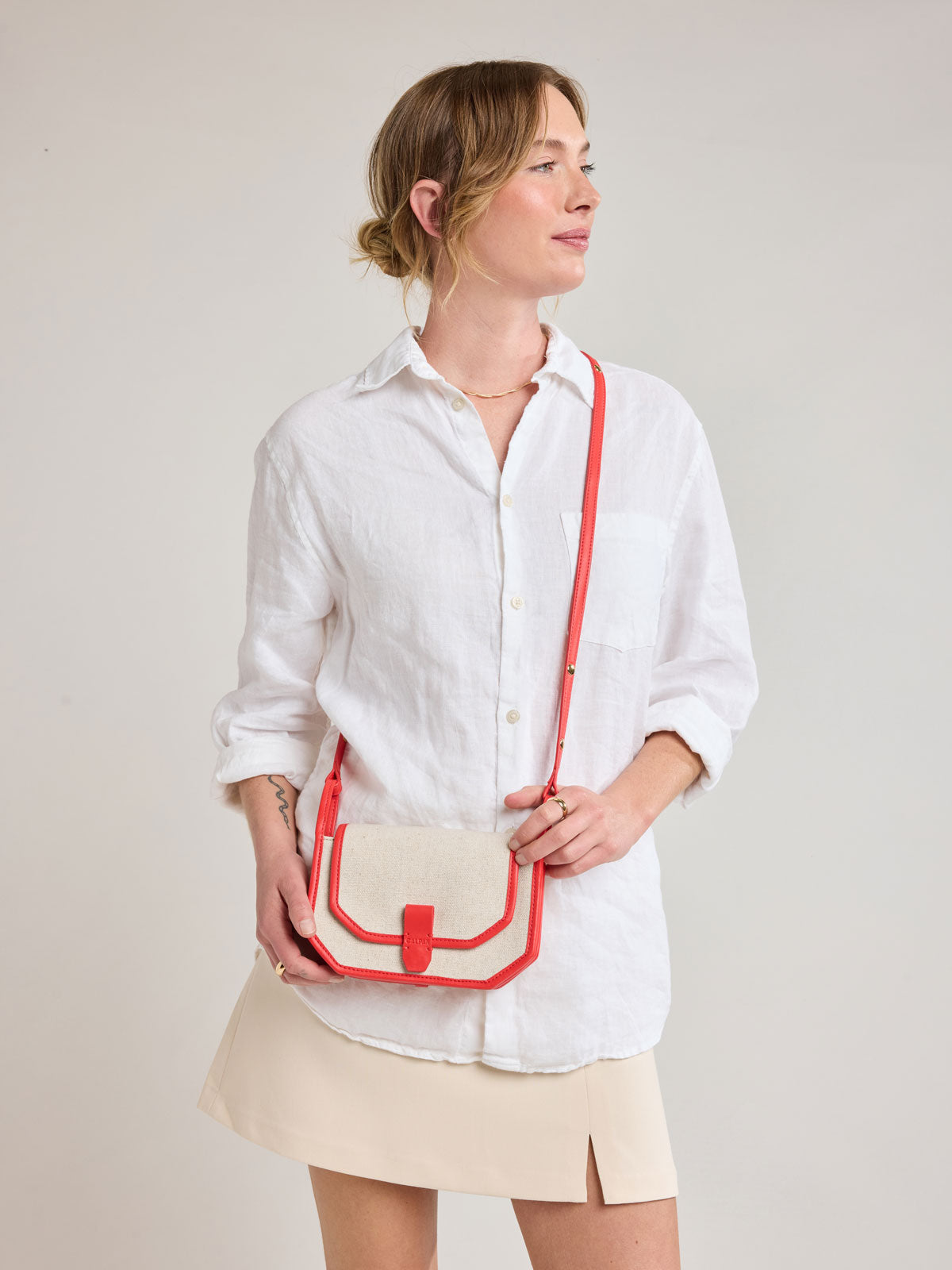 Woman wearing CALPAK Colette Canvas Crossbody Wallet Bag in Natural Brown with beige canvas material and red finishing; CLWC2601-NATURAL-TOMATO