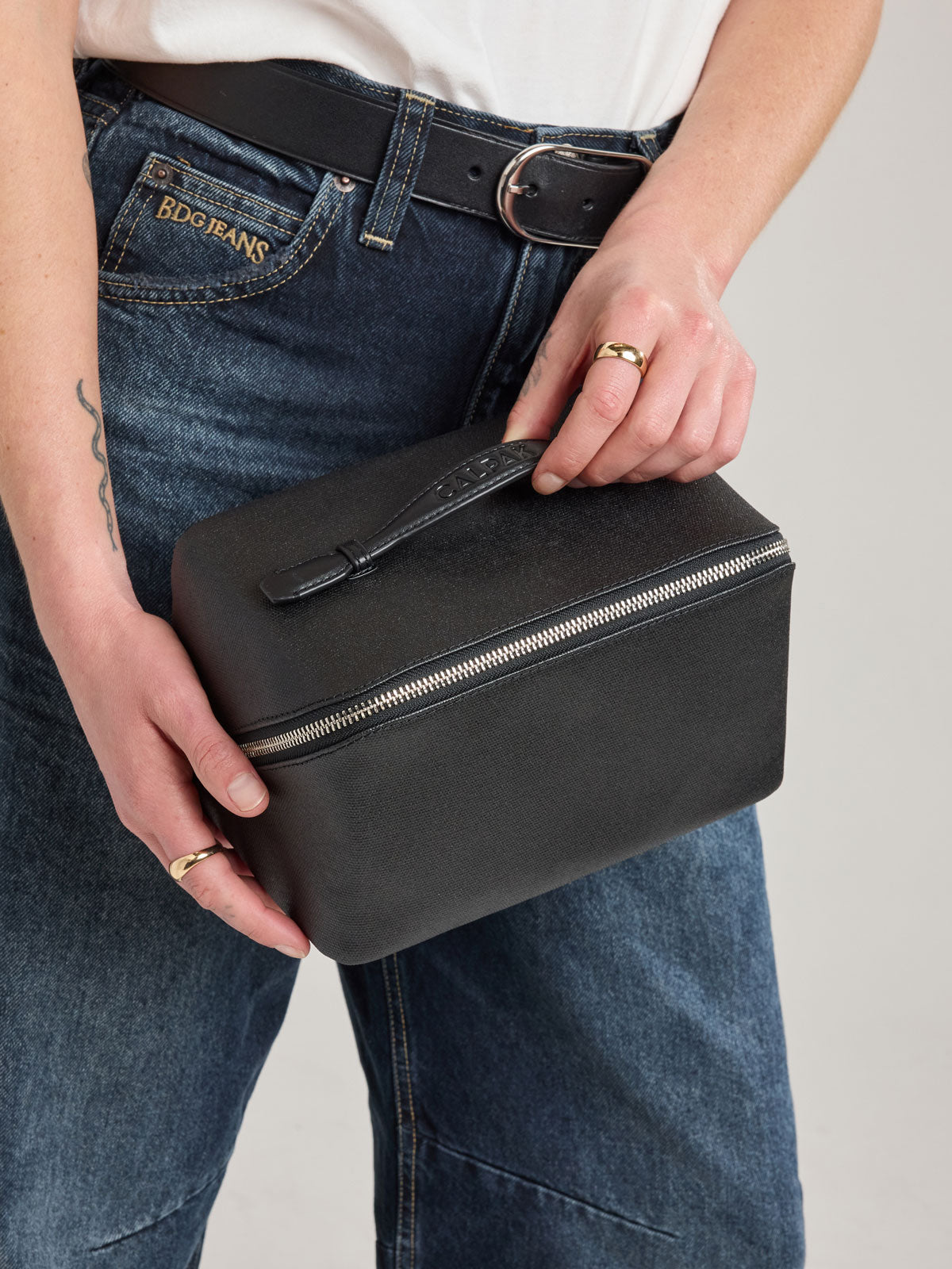 Woman holding CALPAK Colette Lay-Flat Canvas Toiletry Bag in canvas  black material; CLTB2601-BLACK