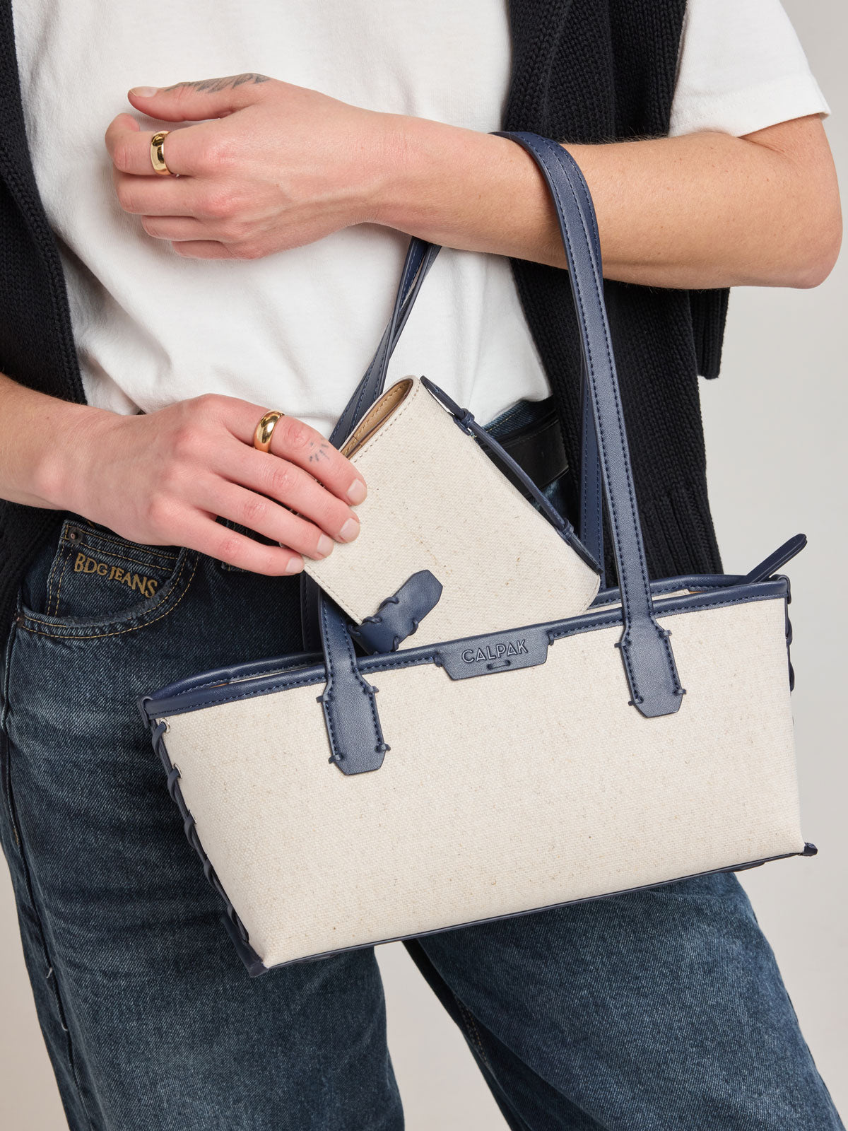 Model putting in bag the CALPAK Colette Multi Passport Wallet in beige canvas material and blue finishings in Natural Navy; CLPW2601-NATURAL-NAVY