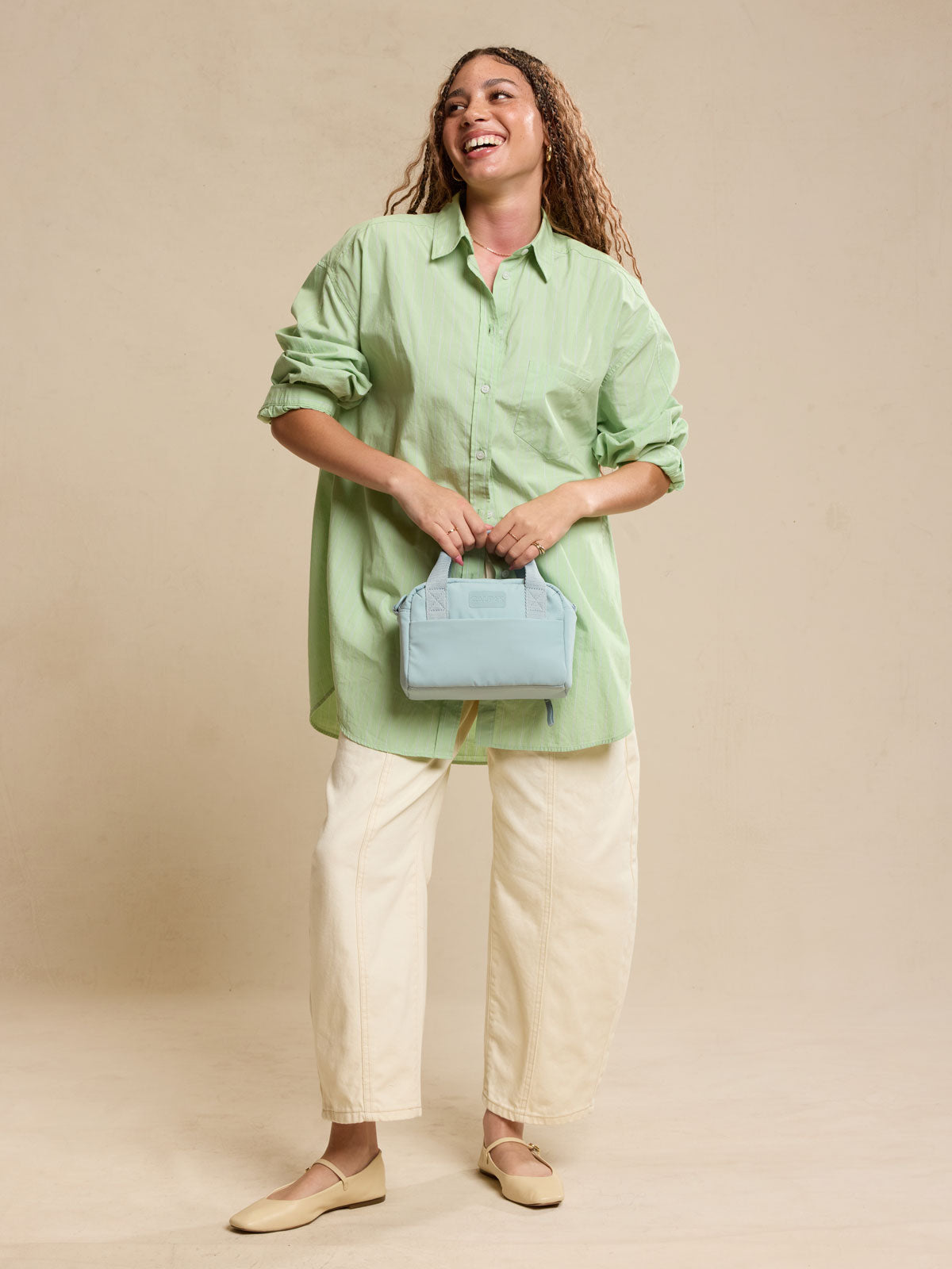 CALPAK Connect Crossbody Bag with adjustable strap in light blue Bluebell being held by a woman against a beige background ; CCN2501-BLUEBELL
