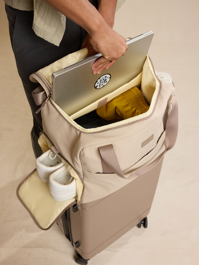 CALPAK Laptop Duffel in beige Greige with model putting a laptop in the duffel against a beige background