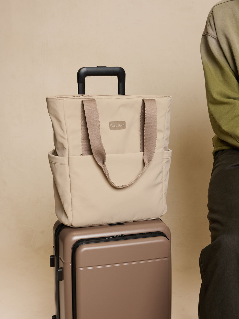 CALPAK Zippered Laptop Tote Bag in beige Greige on a suitcase against a beige background; TCN2501-GREIGE