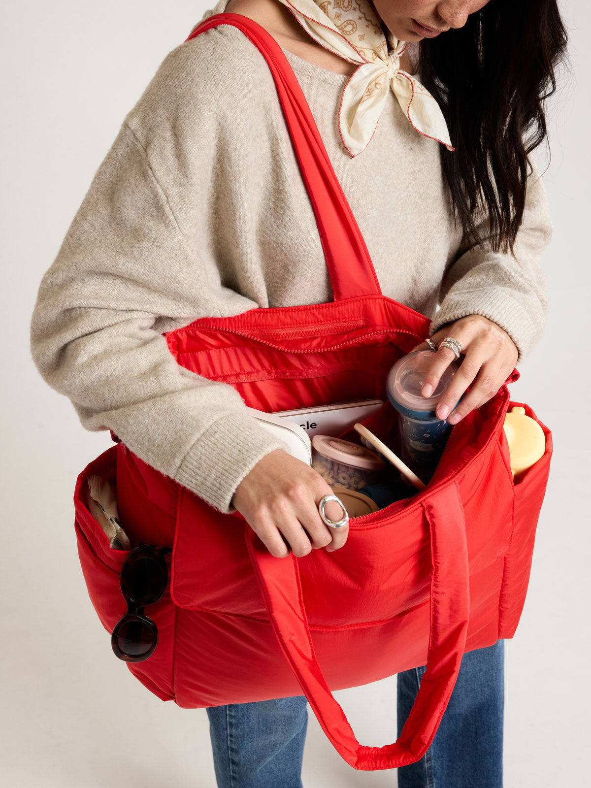 Woman adding items into CALPAK Diaper Tote bag in red Tomato; TBB2401-TOMATO