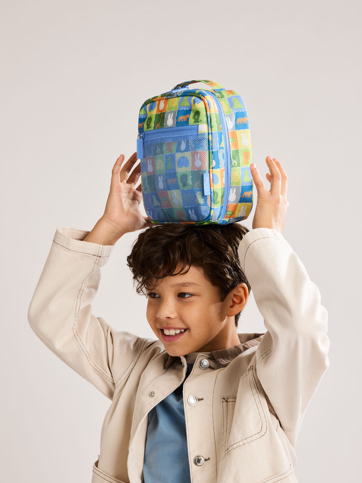 Child holding a colorful organizer with Miffy and zoo animals print for the CALPAK Everything Cube; ACE2401-MIFFY-BLUE-ZOO-TRIP