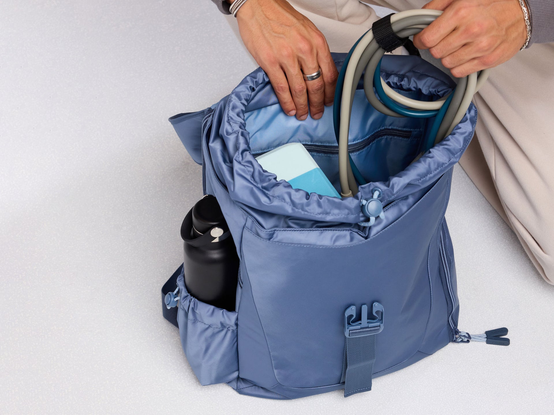 Blue CALPAK Fit Gym Backpack with items being placed inside on a white background