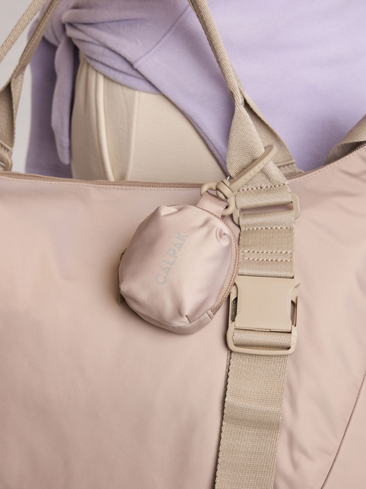 Model holding CALPAK Fit Zip Bag Charm in grey beige Greige with hook and zipper; KPF2601-GREIGE