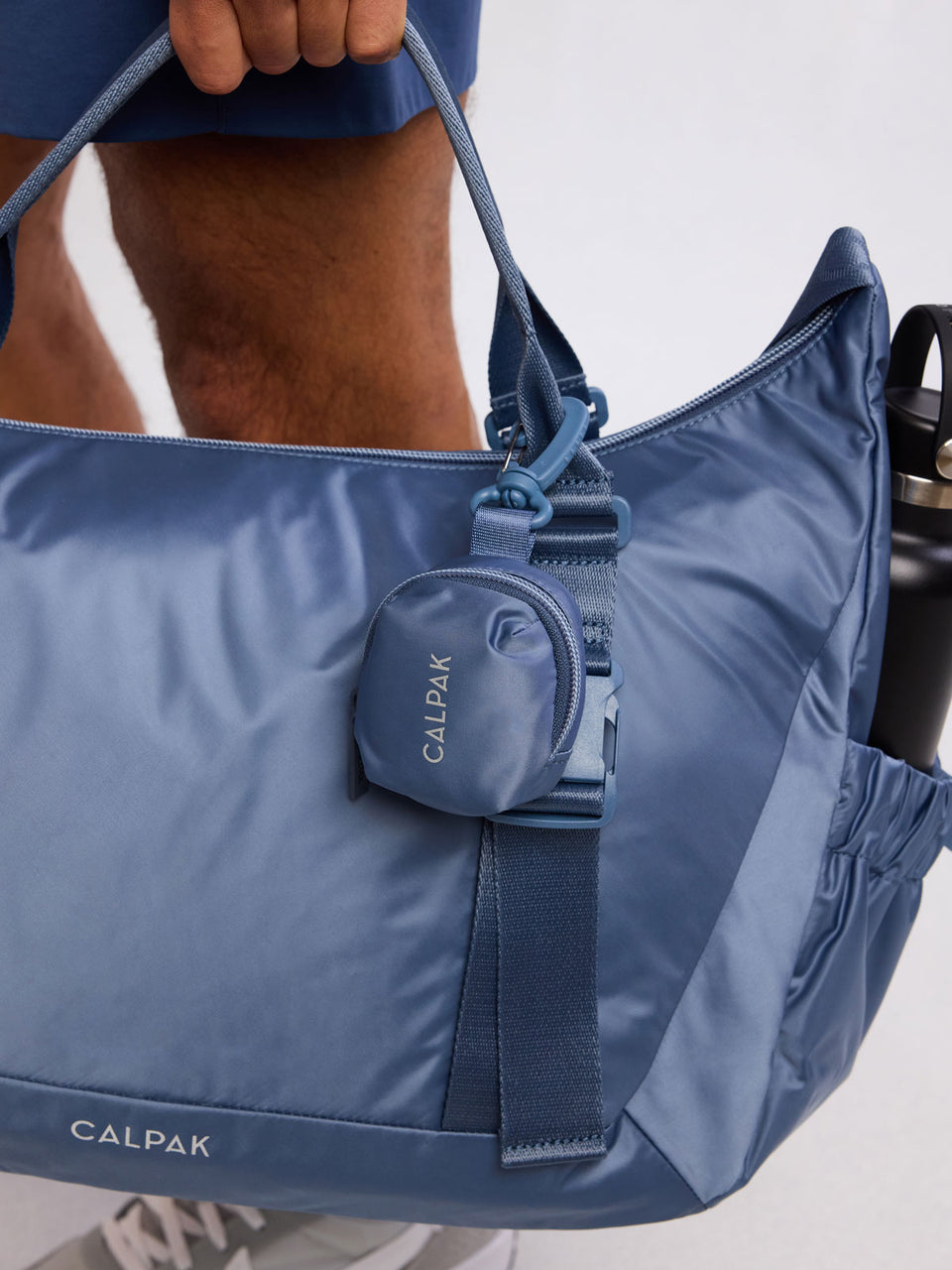 Model holding CALPAK Fit Zip Bag Charm in dark blue Indigo with hook and zipper; KPF2601-INDIGO