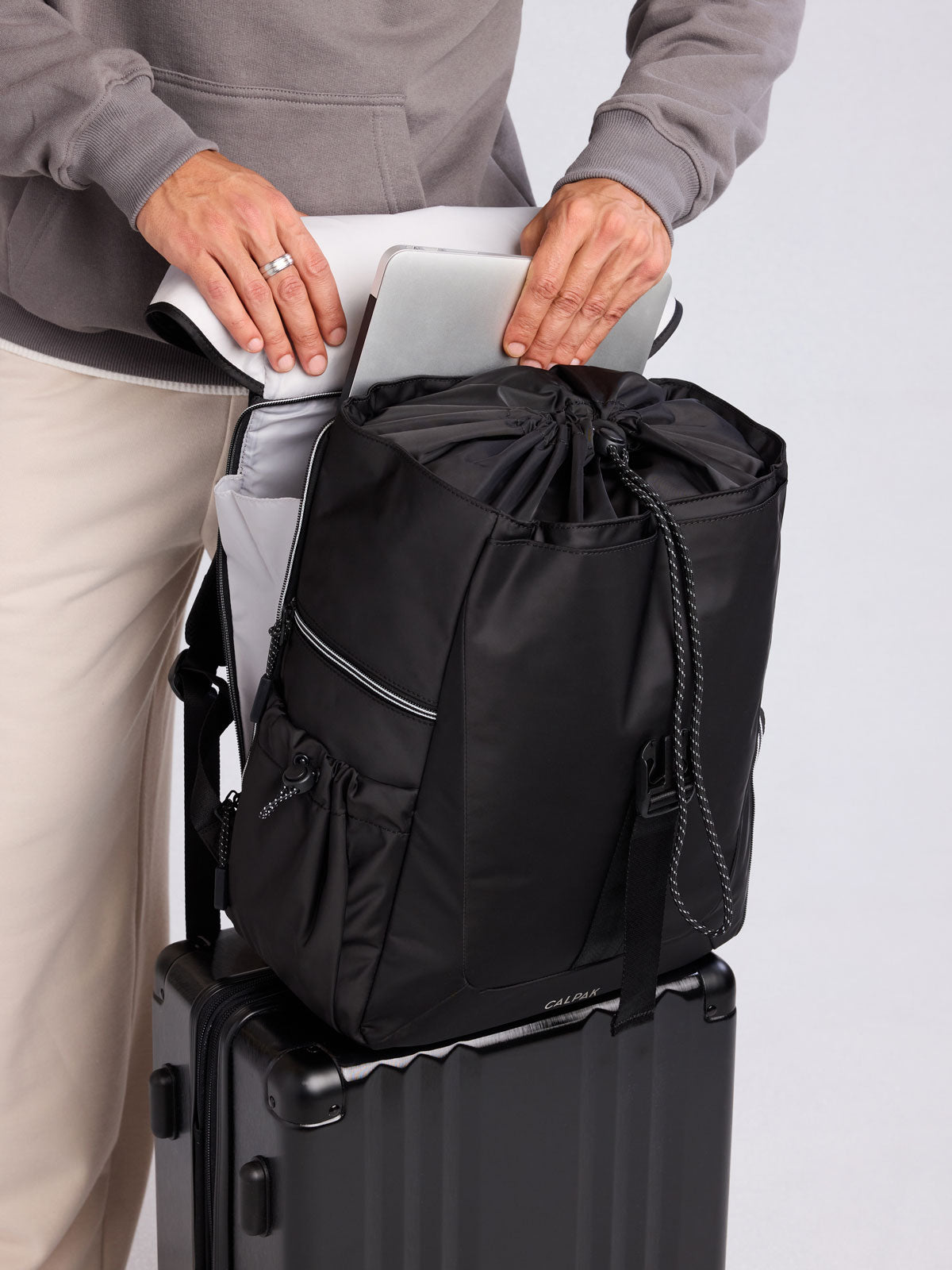 Model using trolley sleeve feature of CALPAK Fit Gym Backpack in Black front view with white background; BPF2601-BLACK