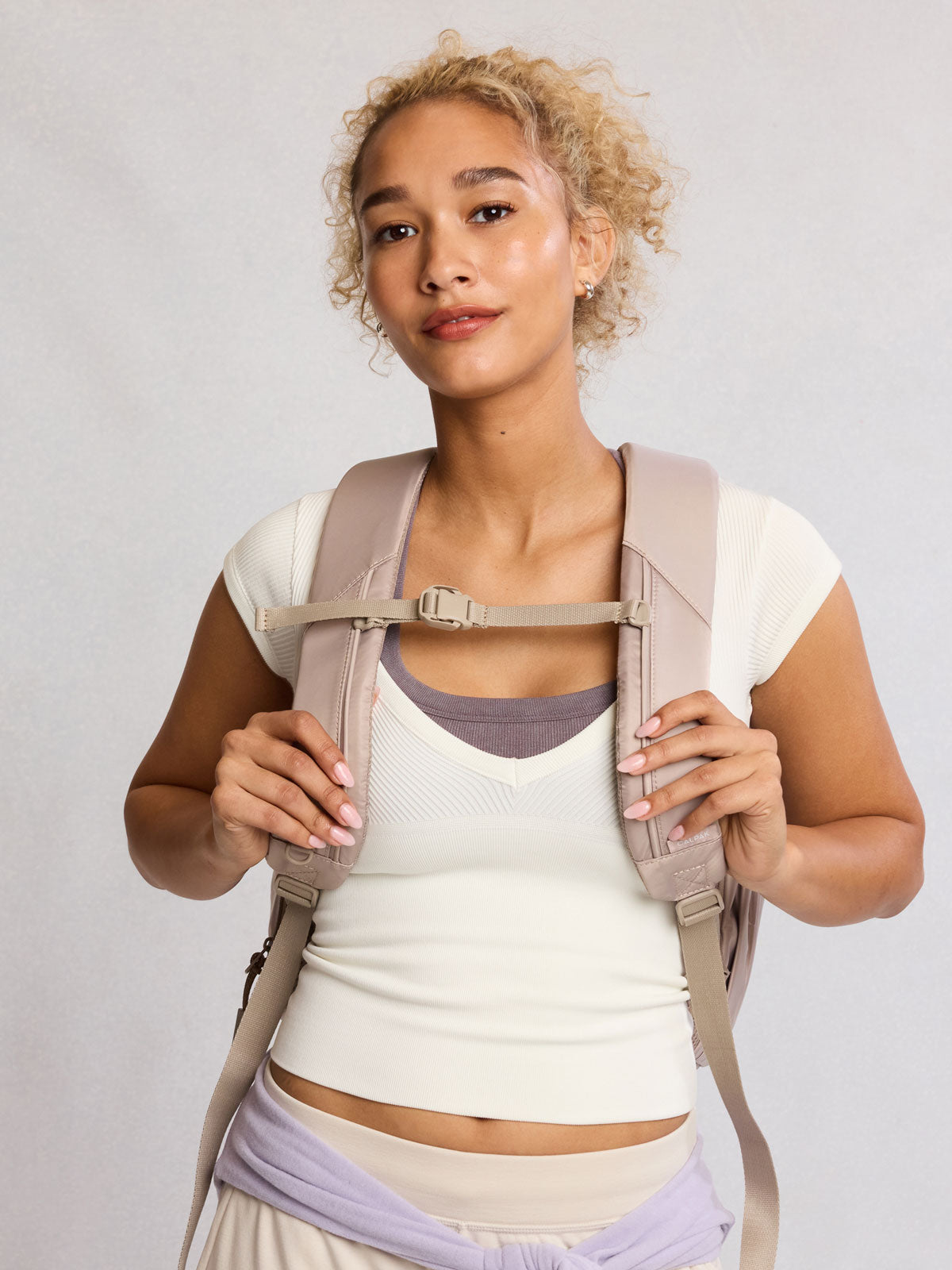 Front view of model wearing CALPAK Fit Gym Backpack in beige Greige front view with white background; BPF2601-GREIGE