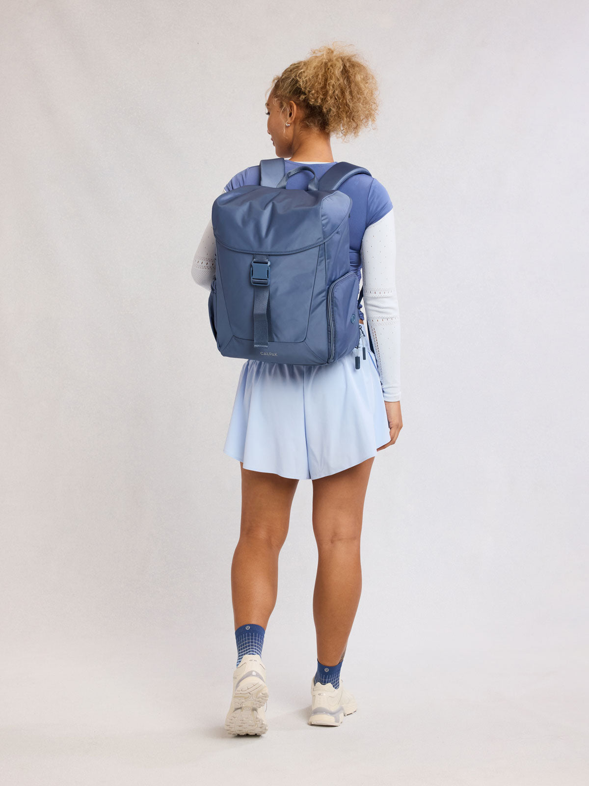 Model wearing CALPAK Fit Gym Backpack in blue Indigo front view with white background; BPF2601-INDIGO
