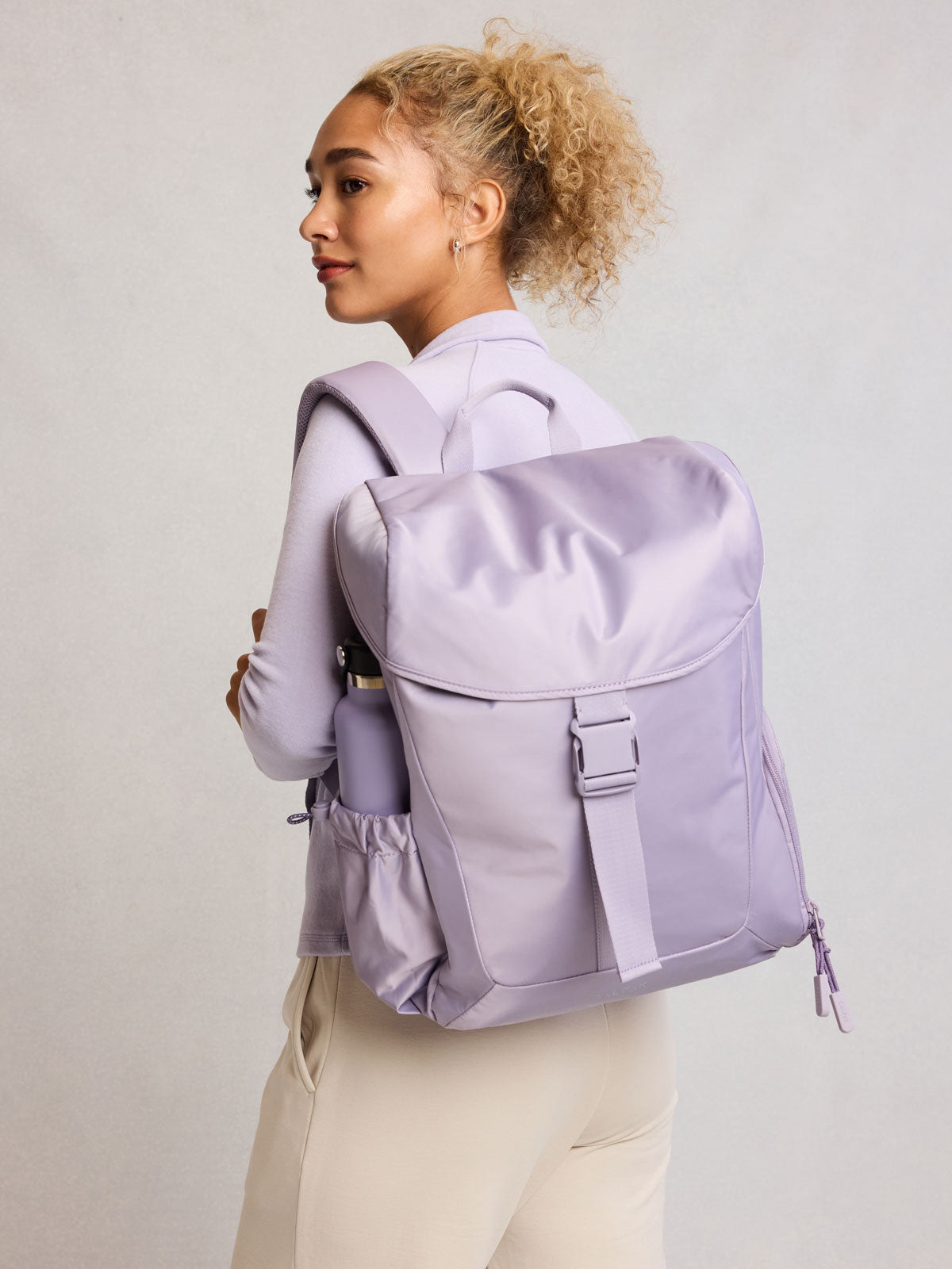 Model wearing CALPAK Fit Gym Backpack in light purple Iris front view with white background; BPF2601-IRIS