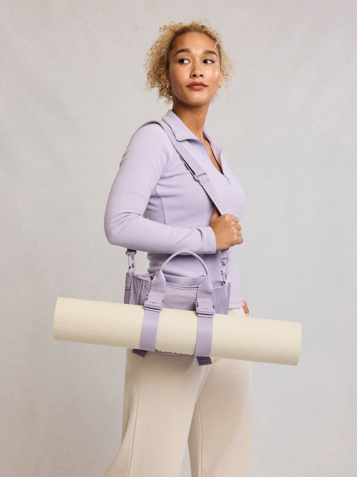 Model wearing CALPAK Fit Gym Crossbody Bag in light purple Iris with Yoga mat attached to front; ABF2601-IRIS