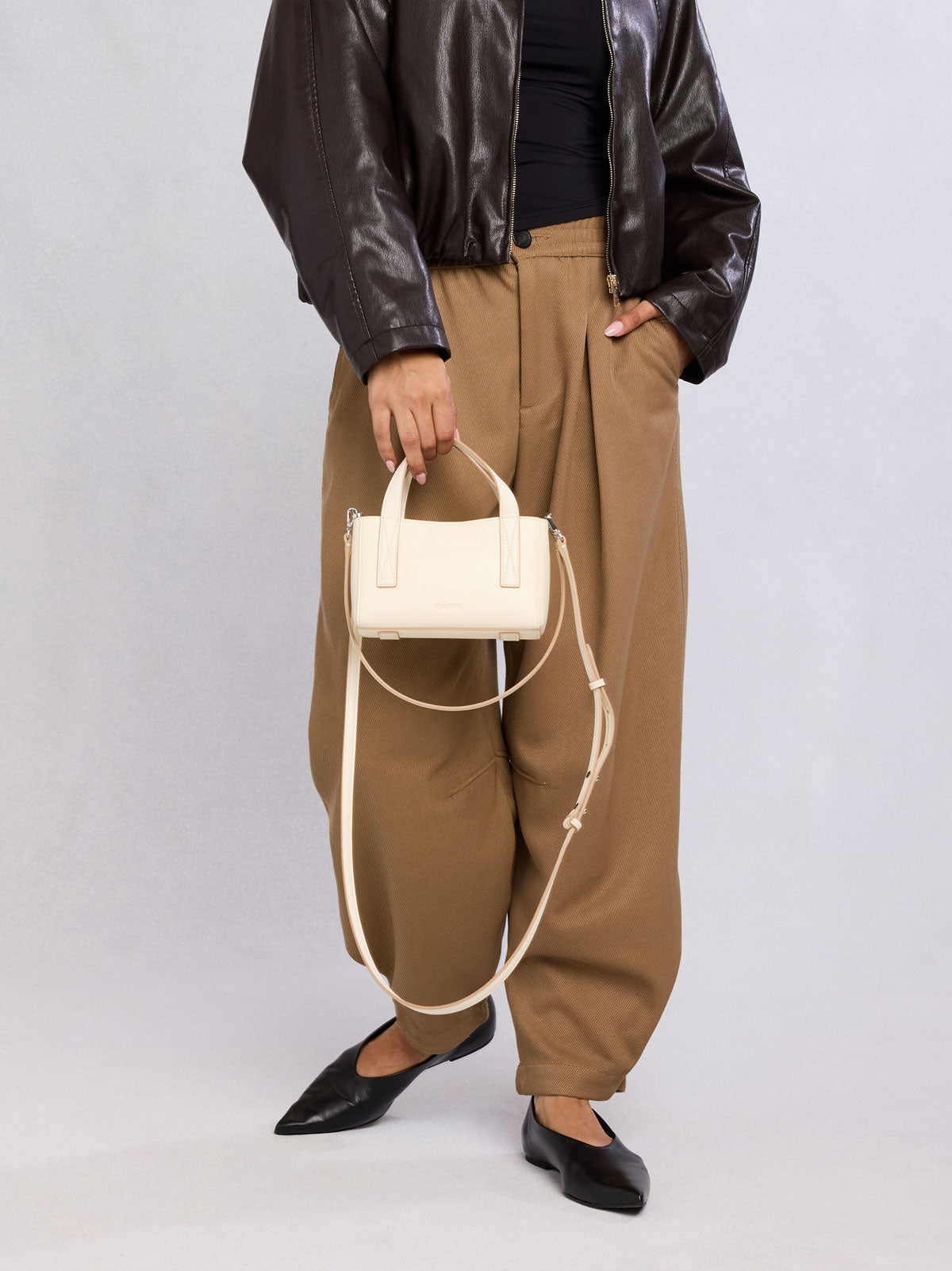 Person holding the CALPAK Haven Mini Crossbody Bag in beige Buttercream; AMC2501-BUTTERCREAM
