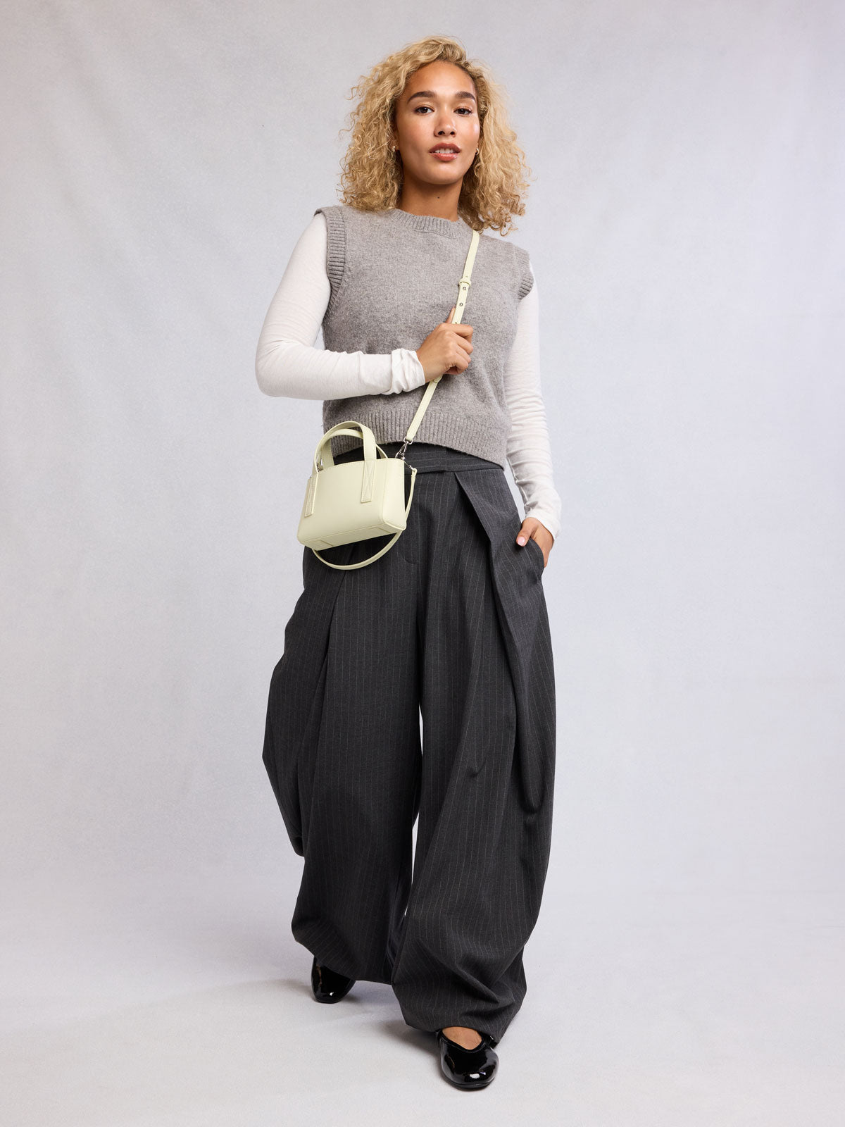 Woman wearing the CALPAK Haven Mini Crossbody Bag in light green Celadon; AMC2501-CELADON