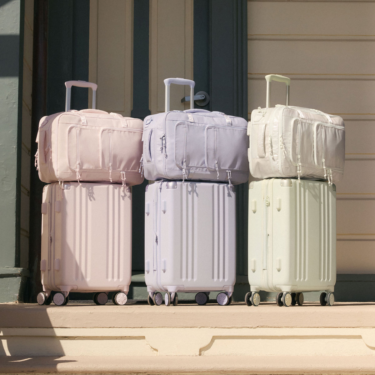 Set of CALPAK Ambeur Suitcases in light green Celadon, purple Sea Glass, and pink Shell Pink with Terra 26L Backpacks matching each suitcase color