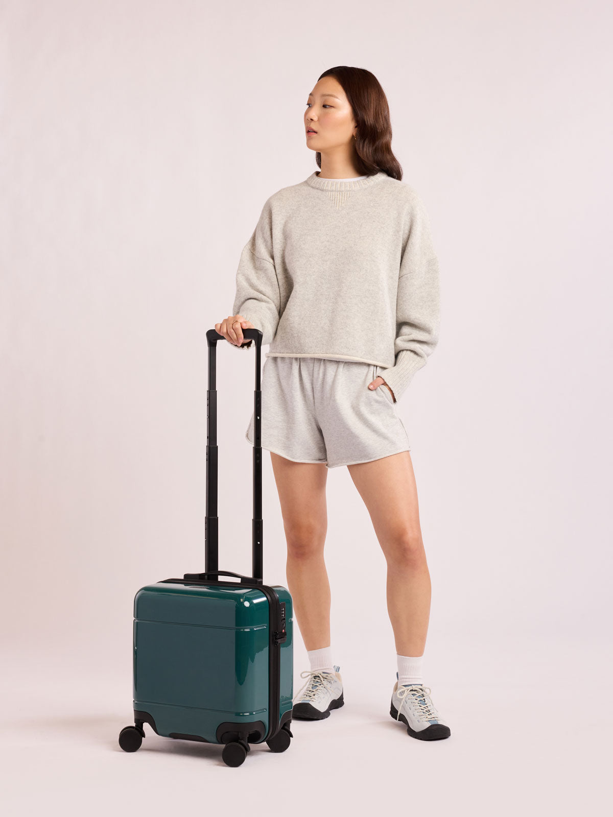 Woman with CALPAK Hue Mini Carry-On Luggage in dark green Kale; LHU1014-GLAZED-KALE