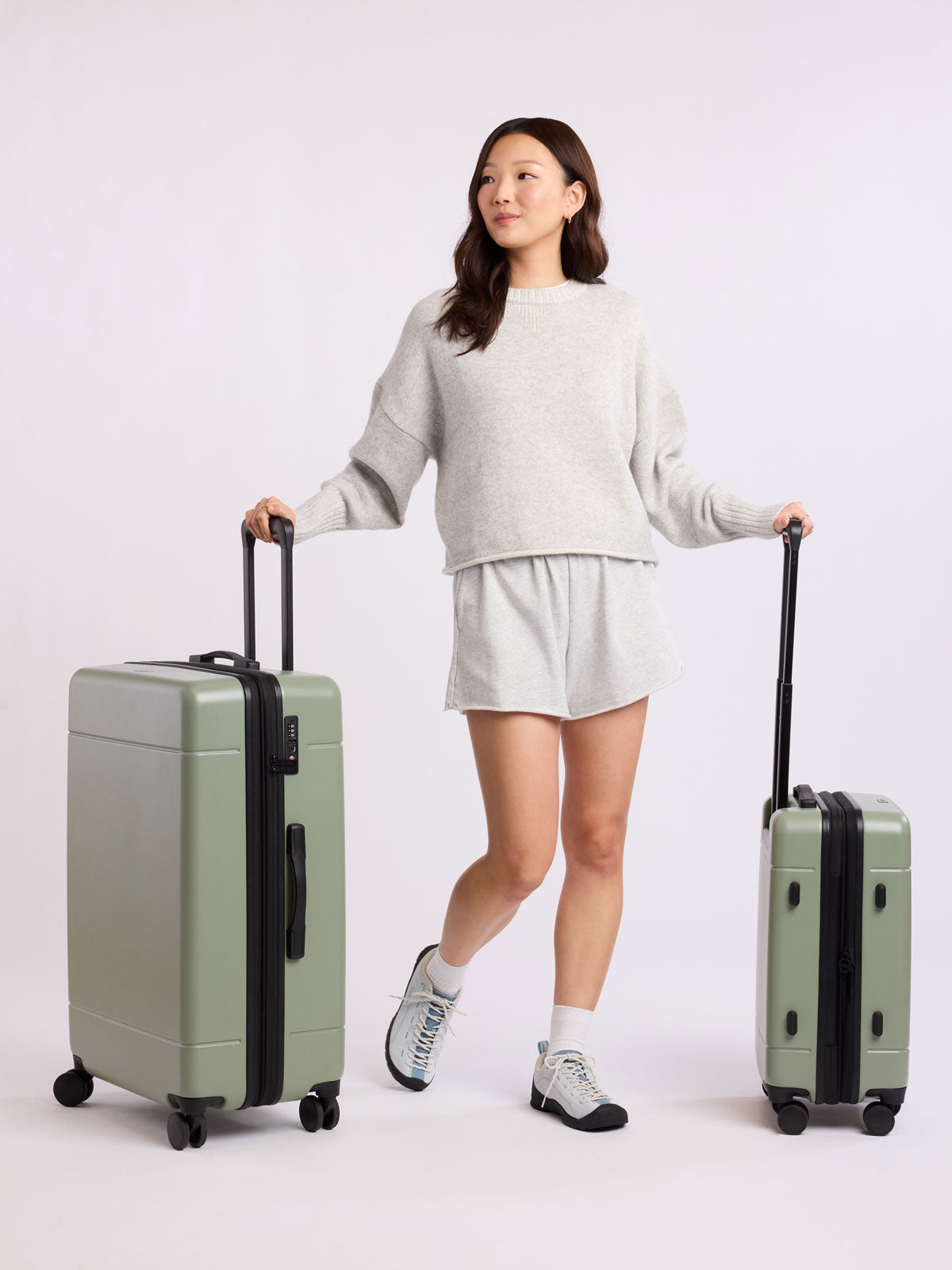 Woman holding two green CALPAK luggage part of Hue Starter Bundle on a white background; LHU8000-JUNIPER