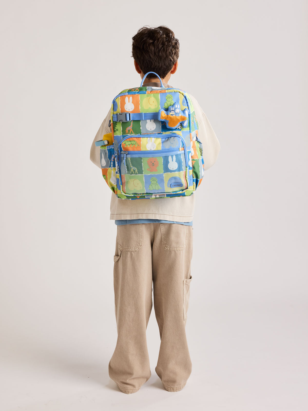 Child wearing the CALPAK Kids Large Backpack with Miffy and blue colorful animal pattern on a white background; CKBL2501-MIFFY-BLUE-ZOO-TRIP