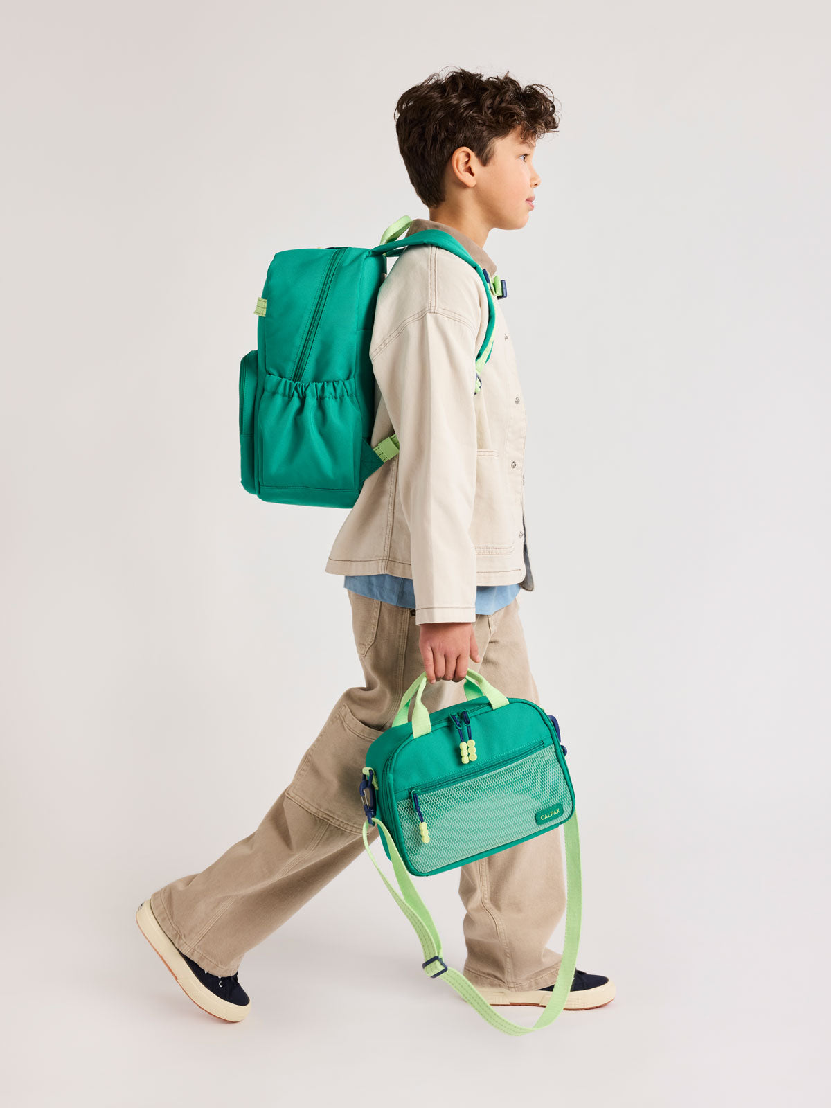 Child wearing a Green CALPAK Kids Medium Backpack  and matching CALPAK Lunch Bag with lime green accents on a white background; CKBM2501-GREEN