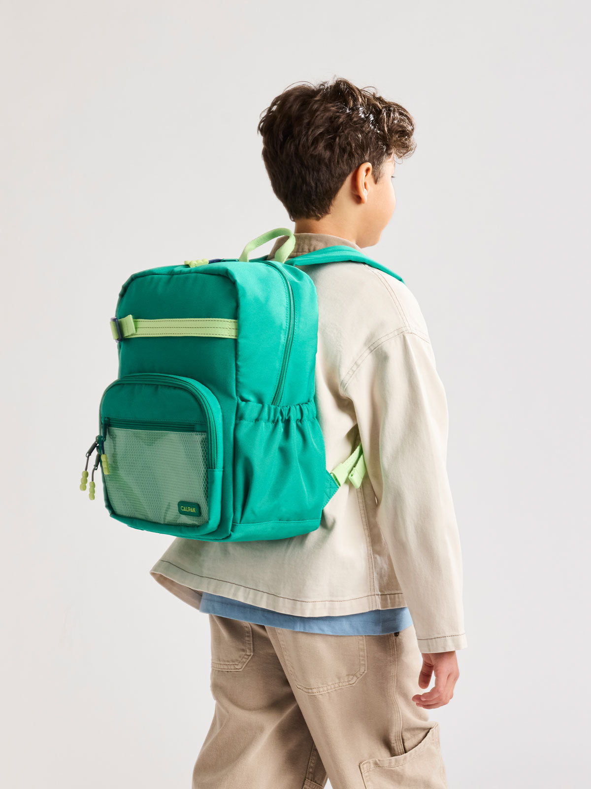 Child wearing a Green CALPAK Kids Medium Backpack with lime green accents on a white background; CKBM2501-GREEN