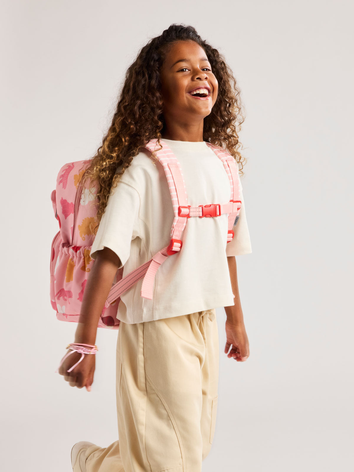 Child wearing a CALPAK Kids Medium Backpack with Miffy and pink colorful animal pattern on a white background; CKBM2501-MIFFY-PINK-ZOO-TRIP
