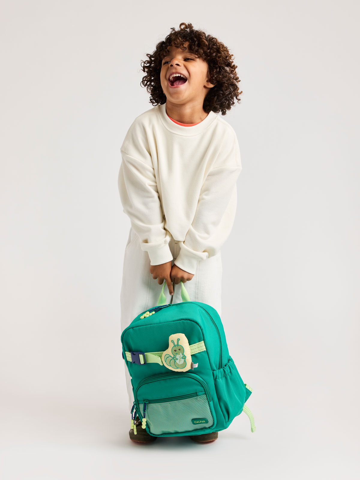 Child holding a Green CALPAK Kids Small Backpack with lime green accents on a white background; CKBS2501-GREEN