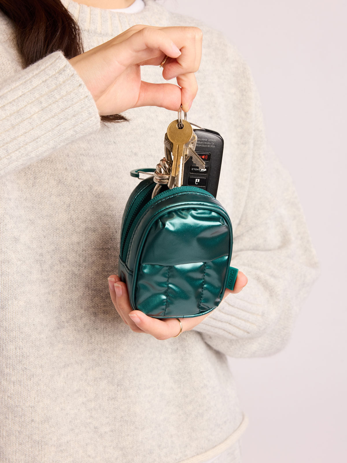 Person putting keys into the CALPAK Luka Backpack Zip Bag Charm in dark green KALE; AMB2201-GLAZED-KALE
