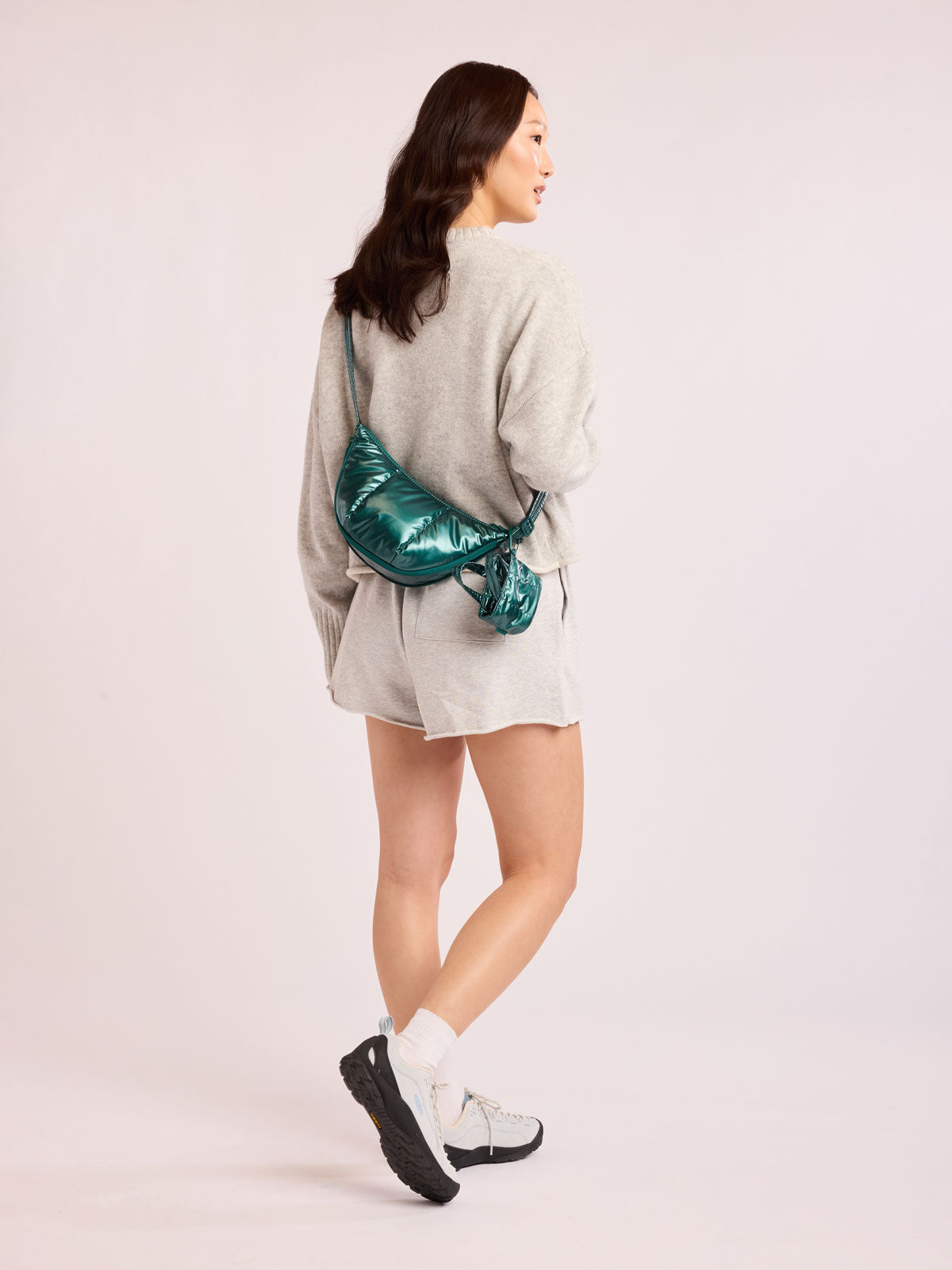 Woman wearing CALPAK Luka Crescent Bag in dark green shiny Kale; CBL2601-GLAZED-KALE